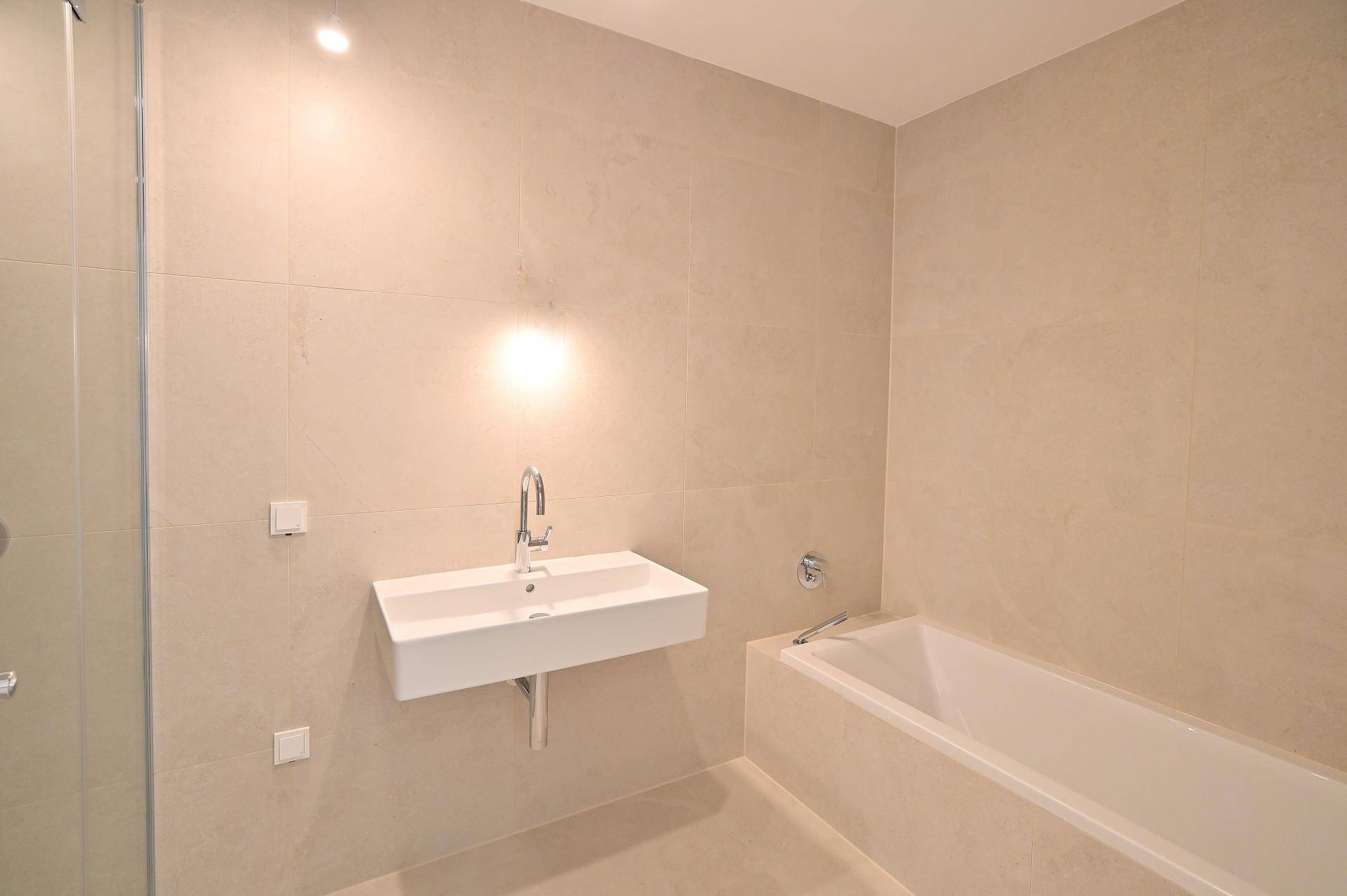 Modernes Badezimmer mit beigefarbenen Fliesen, Waschbecken und Badewanne.