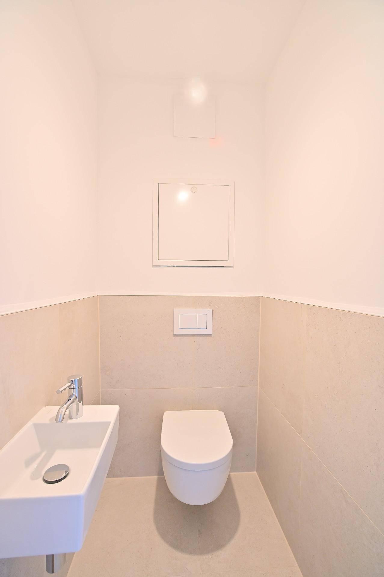 Kleines Gäste-WC mit wandhängendem WC und kompaktem Waschbecken, teilweise gefliest.