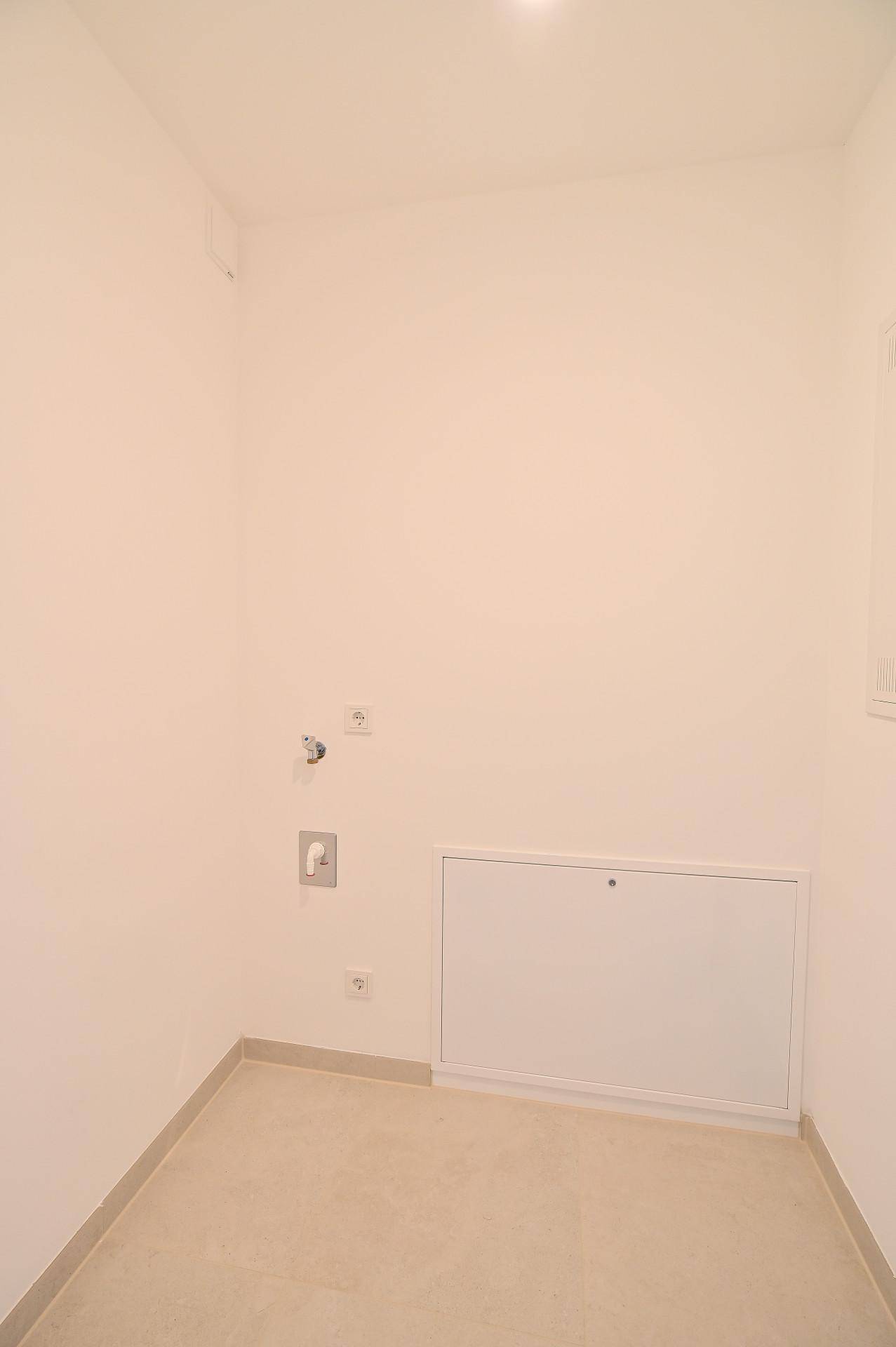 Leerer Hauswirtschaftsraum mit Fliesenboden und Anschlüssen für Waschmaschine.