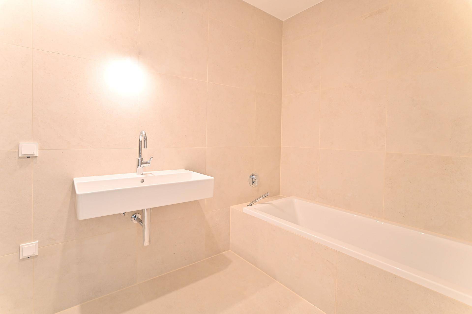 Modernes Badezimmer mit Wandwaschbecken und integrierter Badewanne, komplett gefliest.