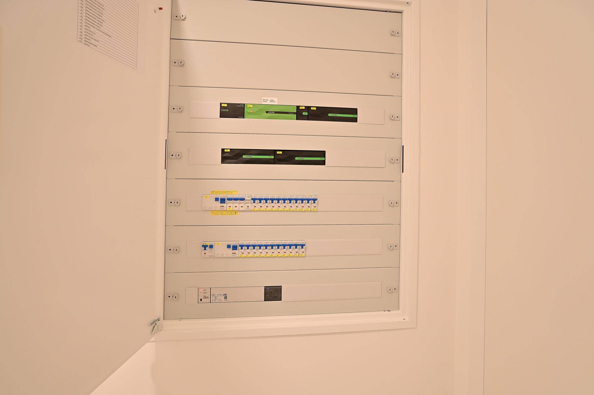 Offener Sicherungskasten mit modernen elektrischen Installationen an einer weißen Wand.