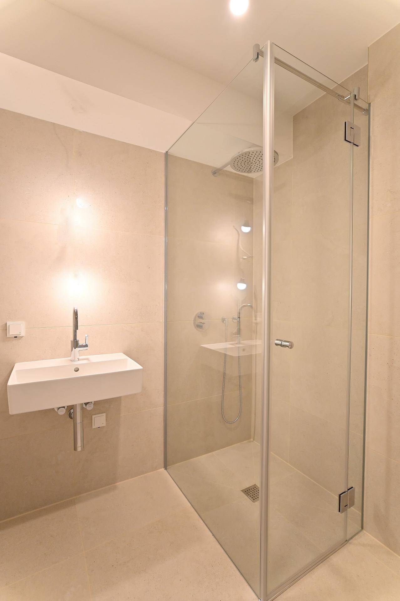 Modernes Badezimmer mit großer Glasduschkabine und schwebendem Waschbecken, in hellen Beigetönen gehalten.