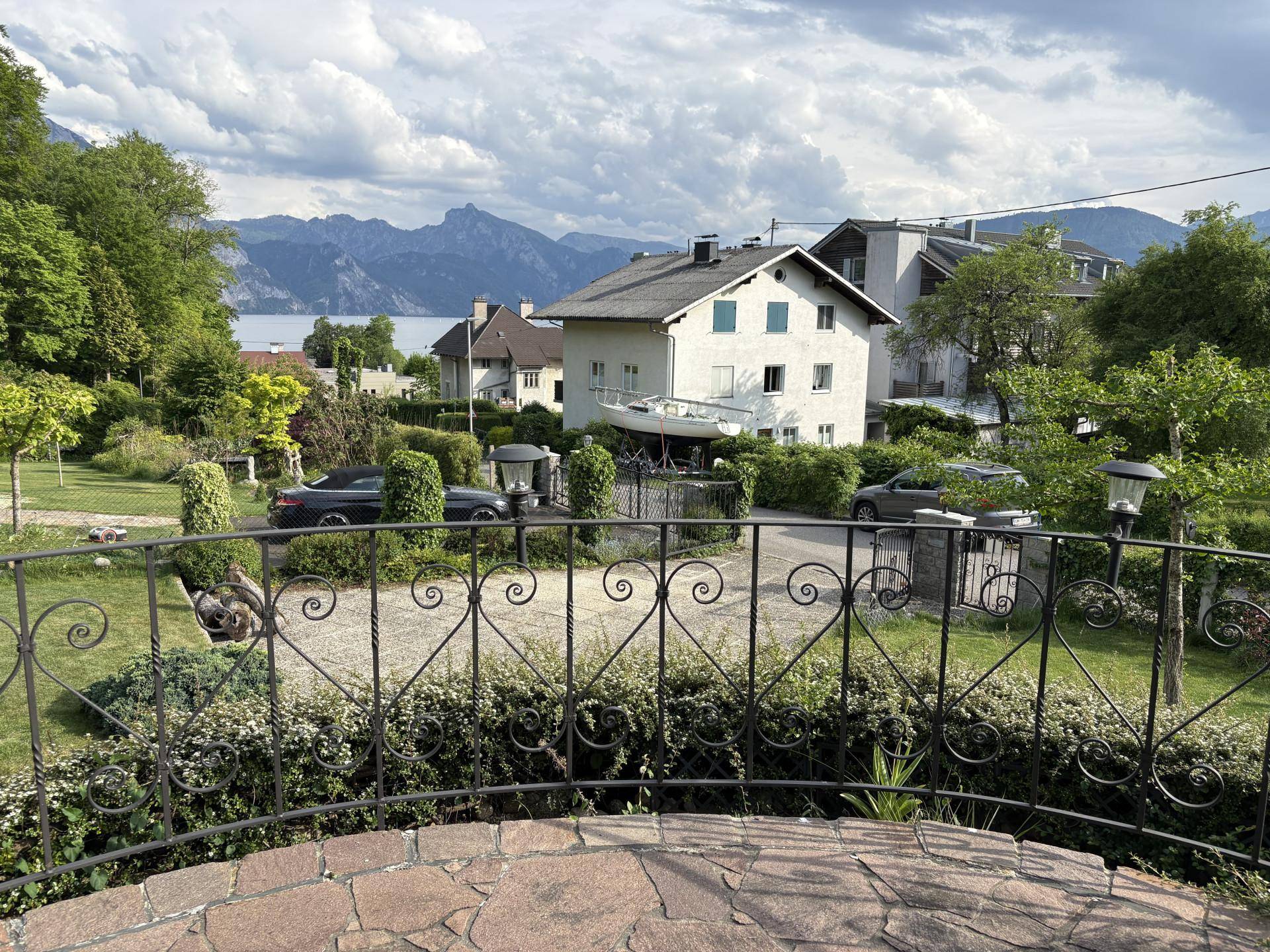 Aussicht von einer Terrasse mit schmiedeeisernem Geländer auf den See und die umliegende Berglandschaft.