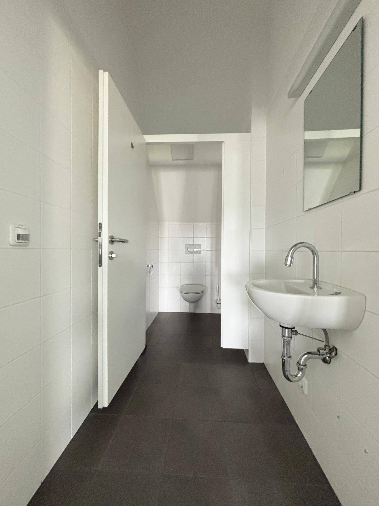 Modernes Badezimmer mit weißen Fliesen, dunklem Boden und einem Waschbecken, das einen sauberen Eindruck macht.
