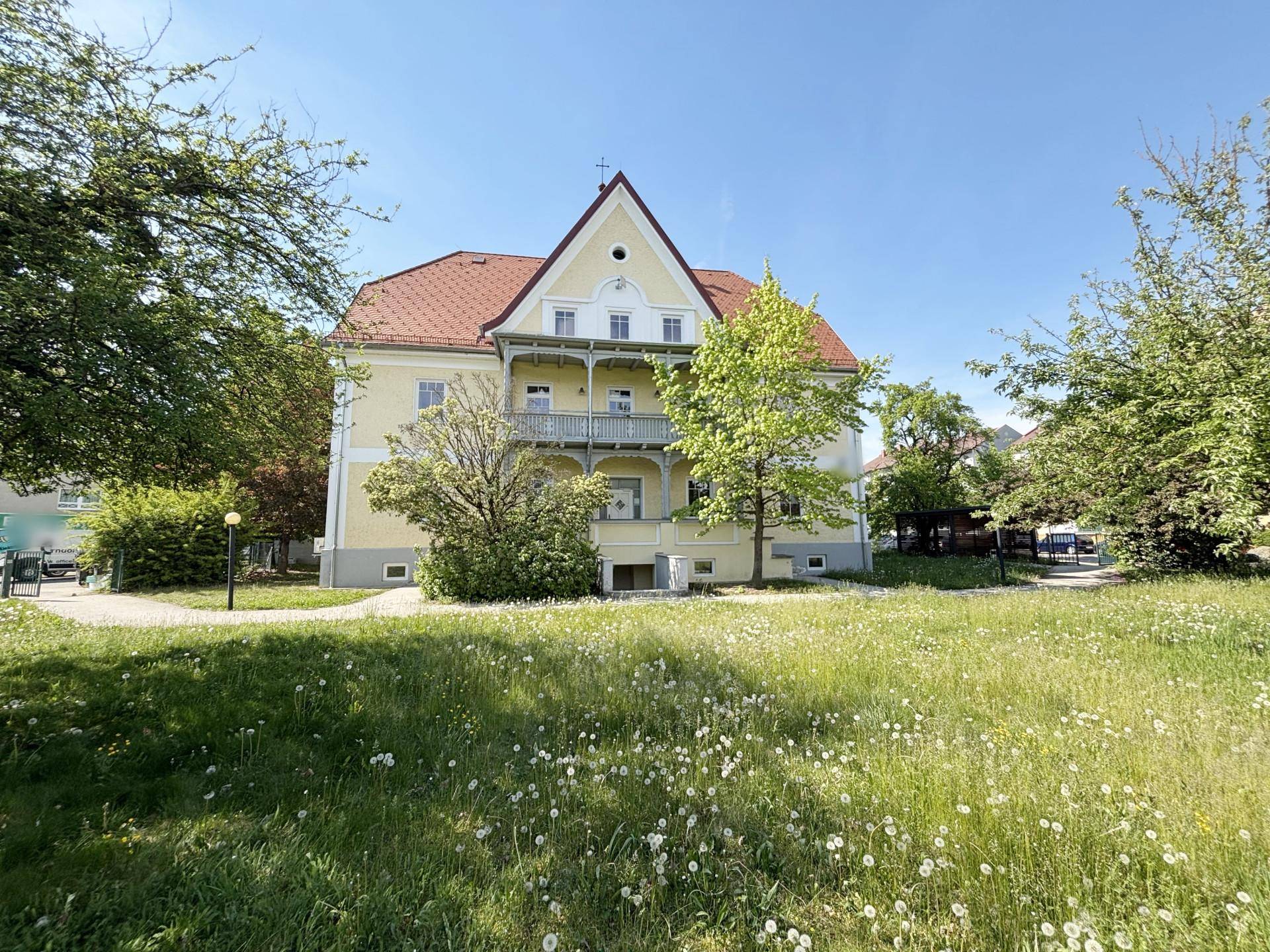 Attraktives Gebäude mit gelber Fassade, rotem Dach und Balkonen, umgeben von grünen Bäumen und Rasenflächen.