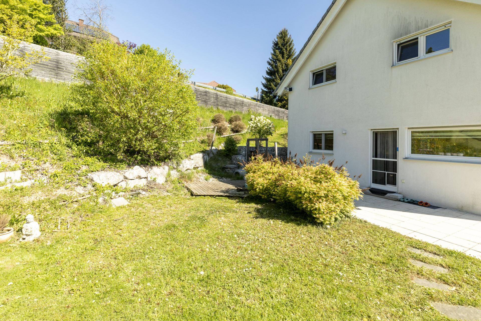 Kleiner Gartenbereich mit Rasenfläche und Sträuchern, angrenzend an eine gepflasterte Terrasse.
