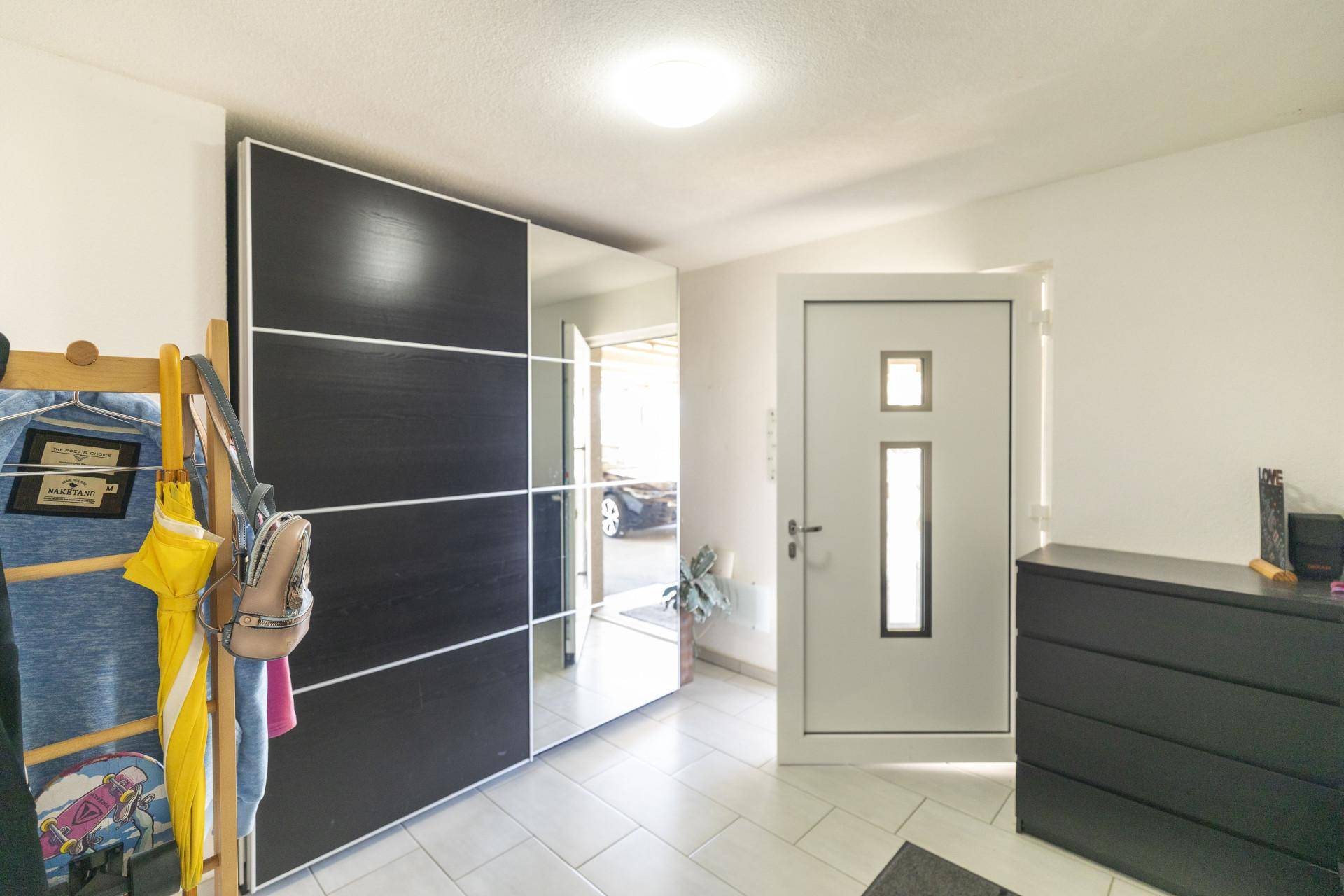 Heller Eingangsbereich mit Fliesenboden, Spiegelschrank und moderner Haustür.