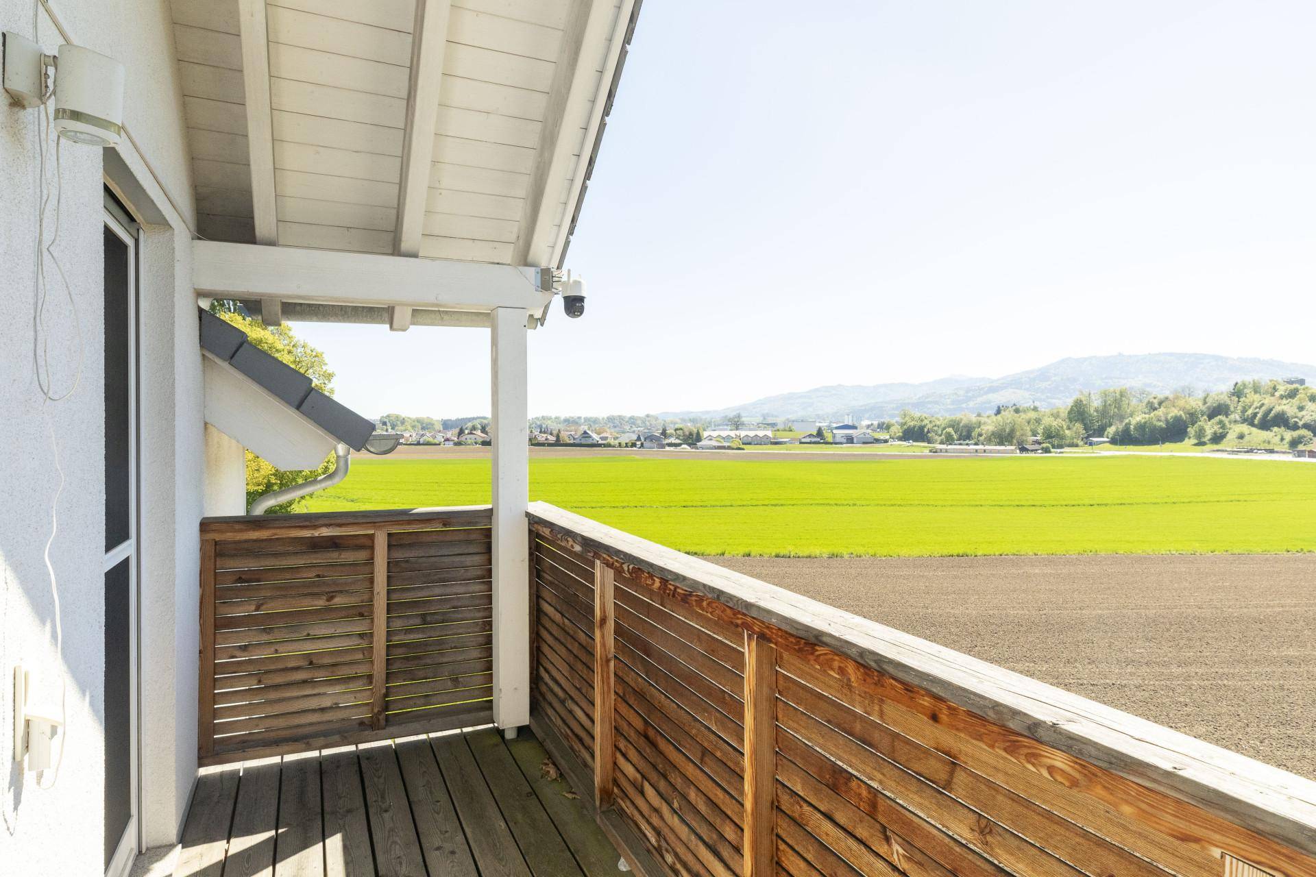 Kleiner überdachter Balkon mit Holzgeländer und weitem Blick über die Felder.