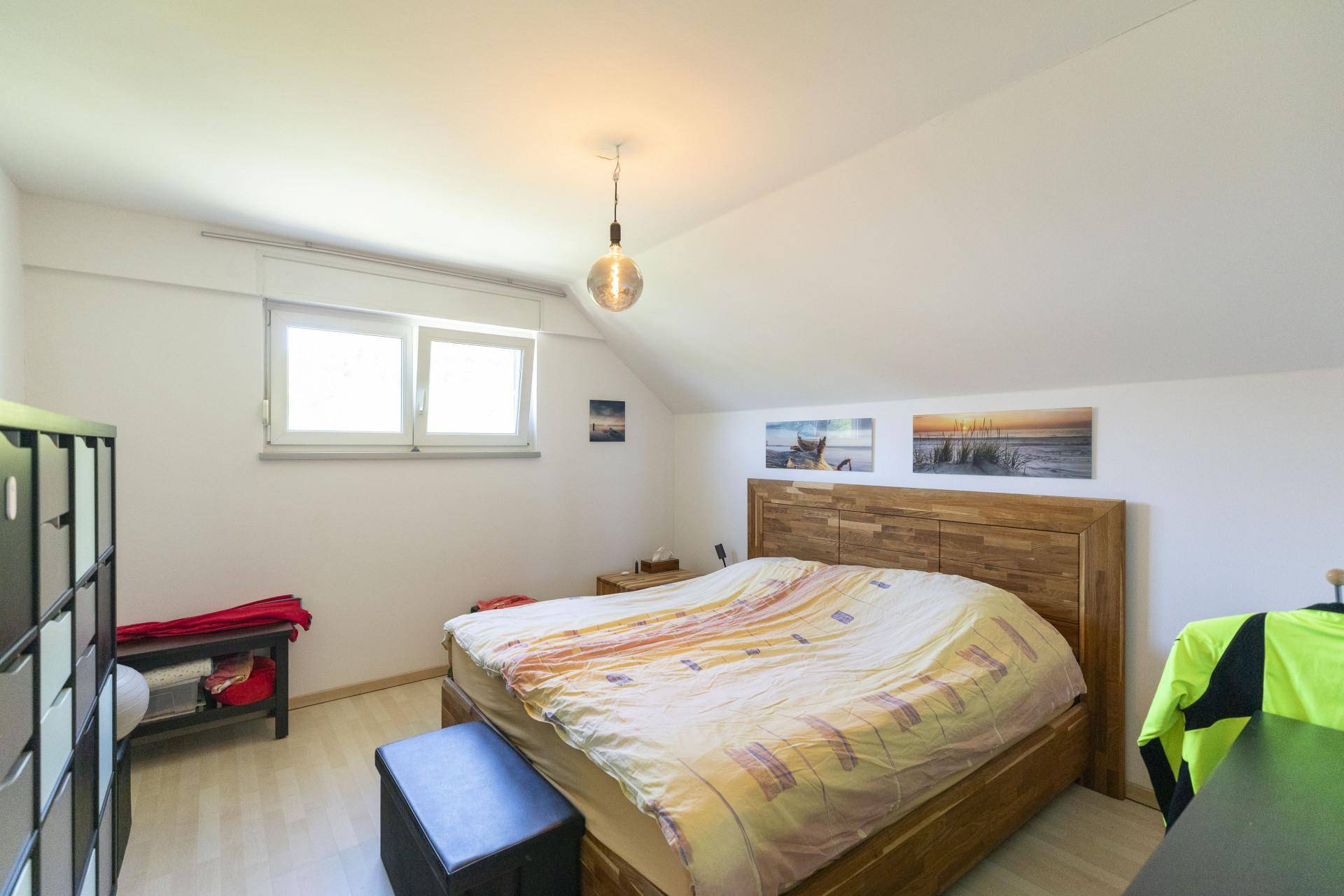 Schlafzimmer mit Holzbett, Dachschräge und Fenster, das viel Tageslicht hereinlässt.