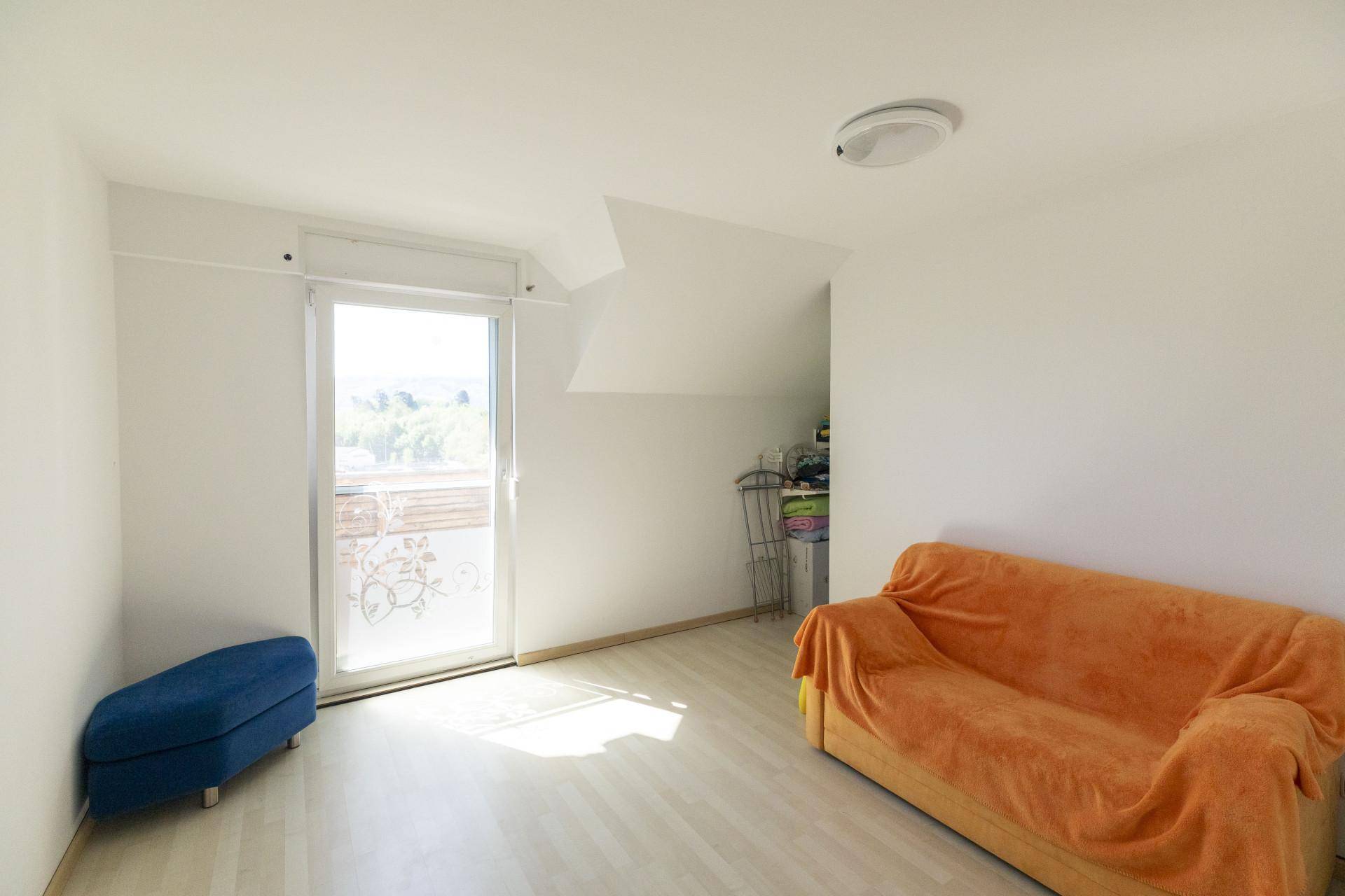 Heller Raum mit Sofa, Fußhocker und Zugang zu einem Balkon, ideal als Gästezimmer.