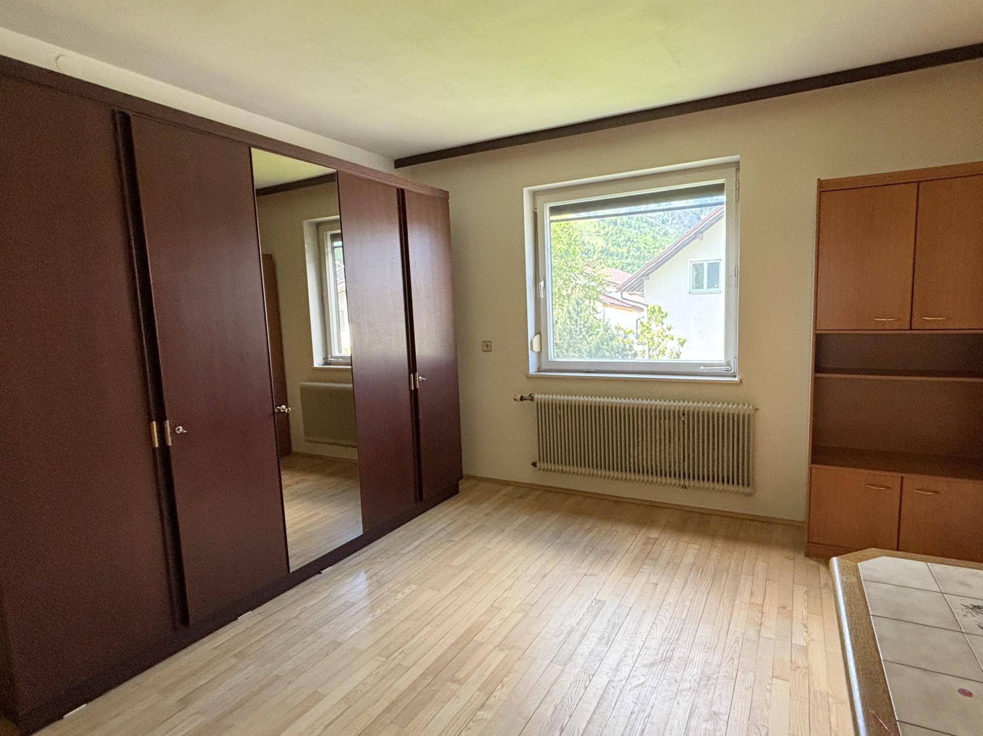 Schlafzimmer mit Holzboden, großem Spiegelschrank und Blick ins Grüne.