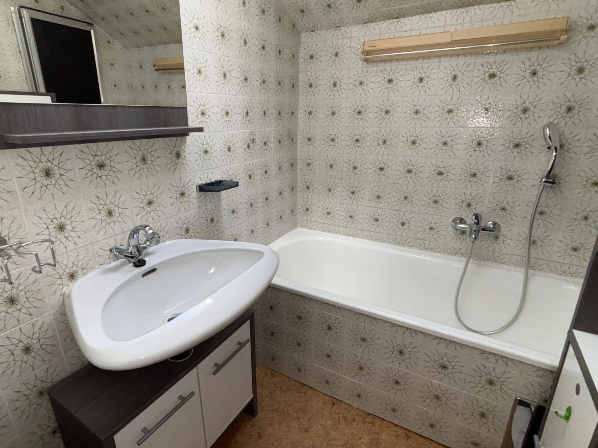 Badezimmer mit Badewanne, Waschbecken und gemusterten Fliesen im Retro-Stil.