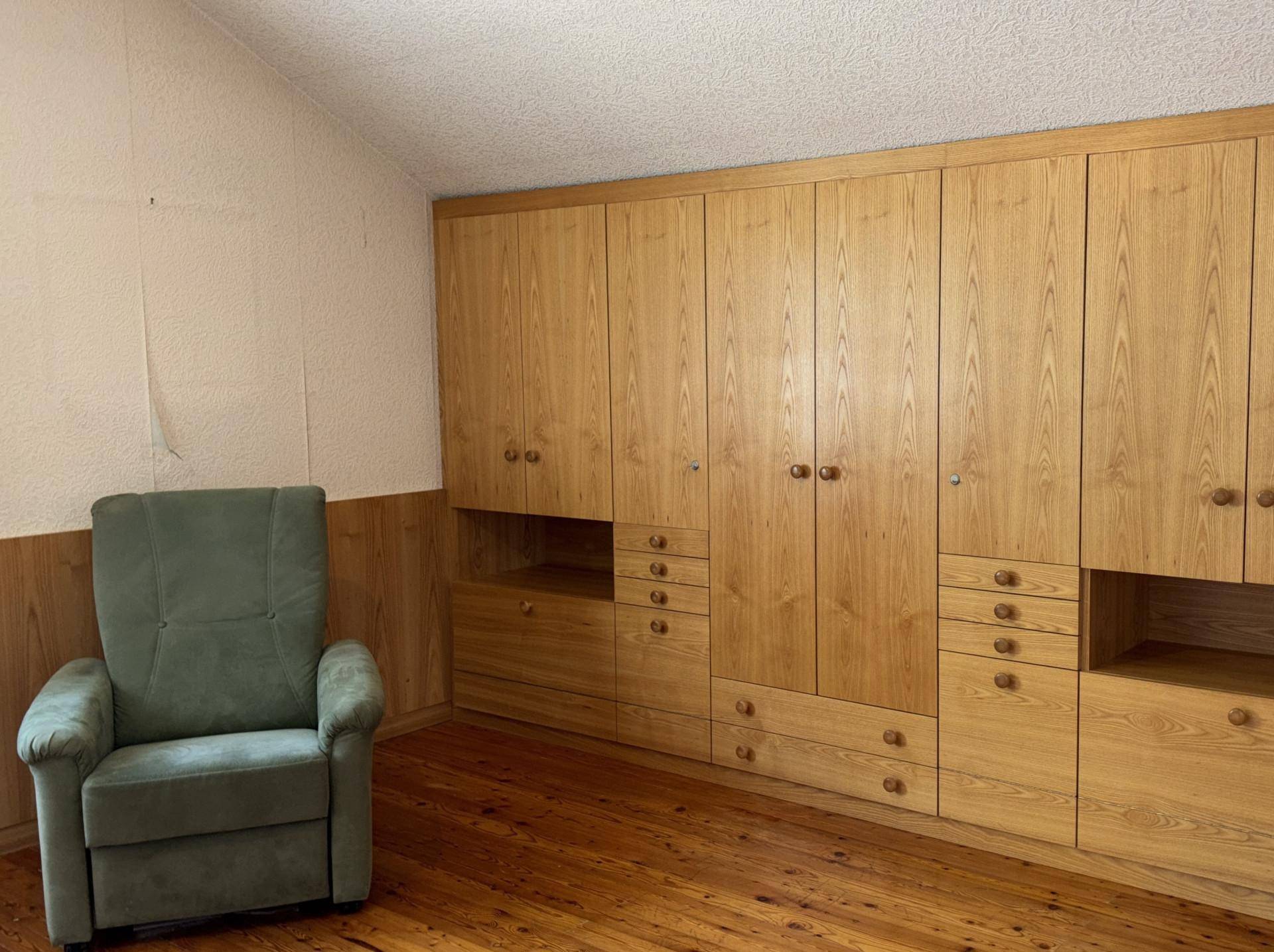 Schlafzimmer im Dachgeschoss mit Einbauschränken aus Holz und Sessel.