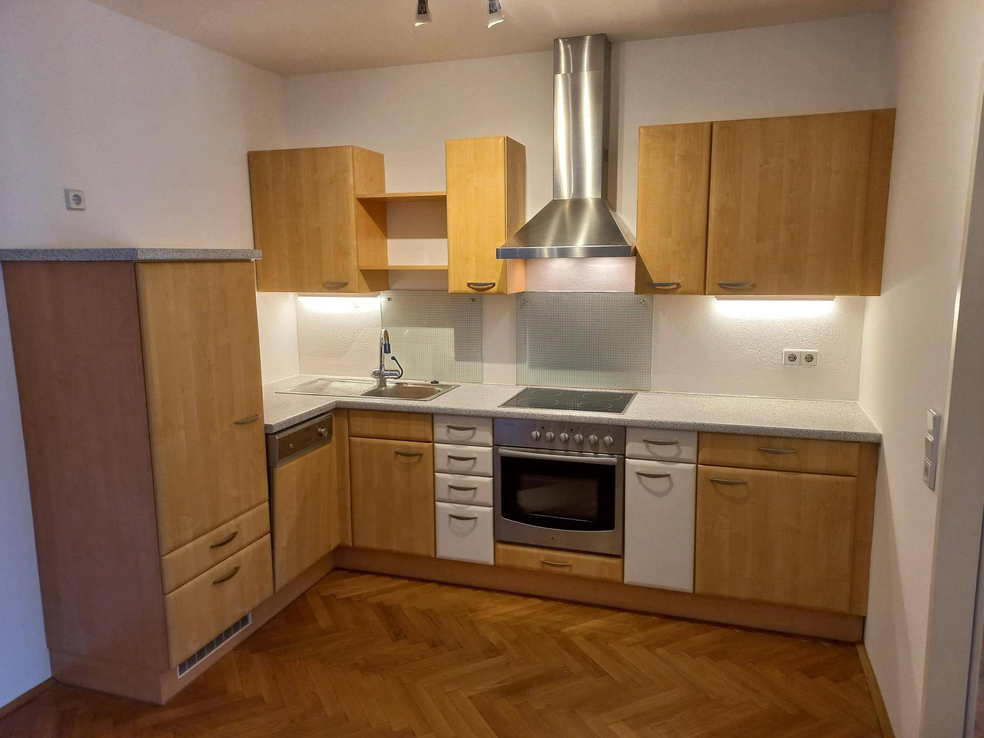 Funktionale Einbauküche mit Holzfronten, integrierten Geräten und Parkettboden.