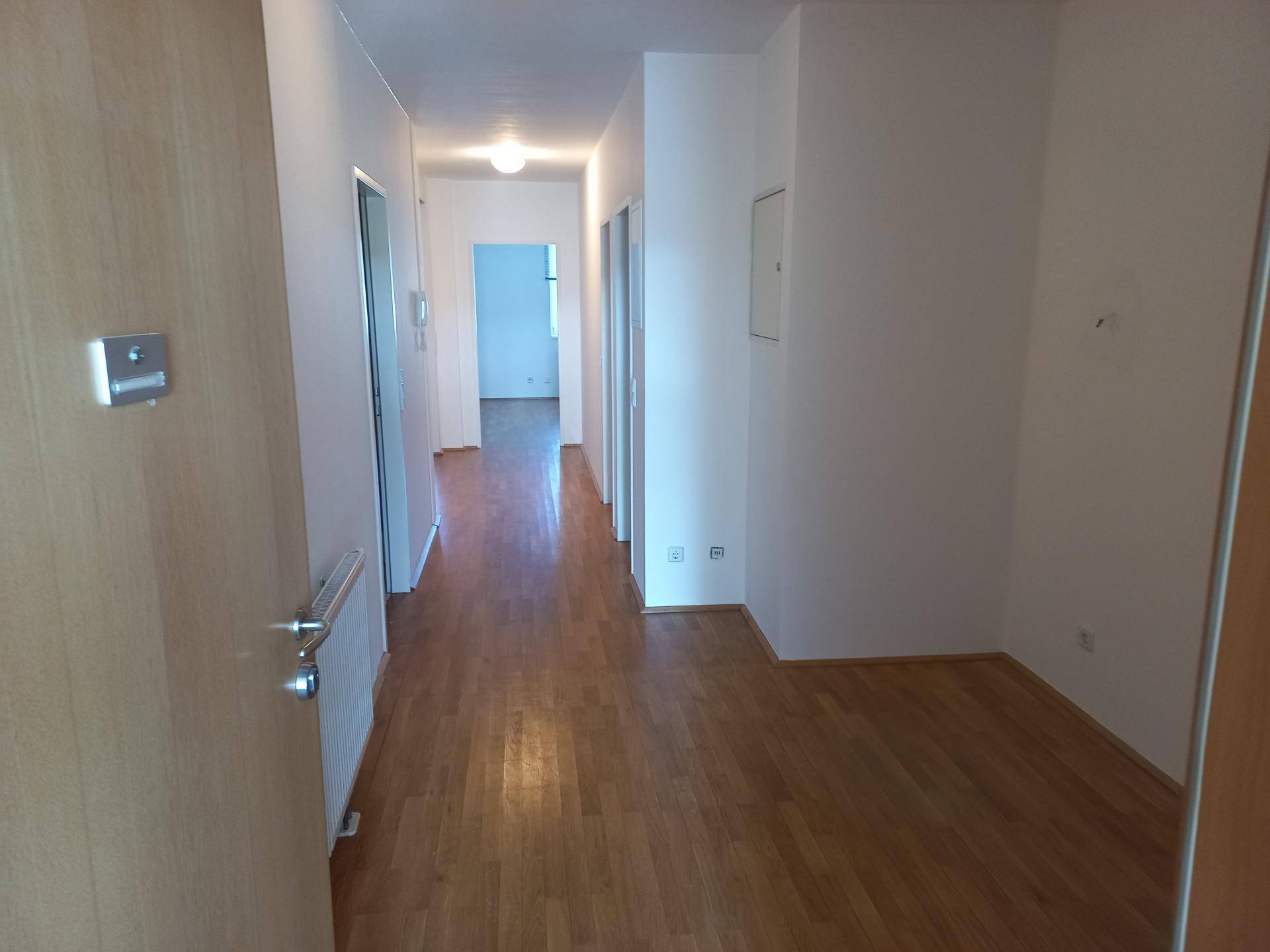 Langer Flur mit Holzfußboden, weißen Wänden und Zugang zu mehreren Zimmern.
