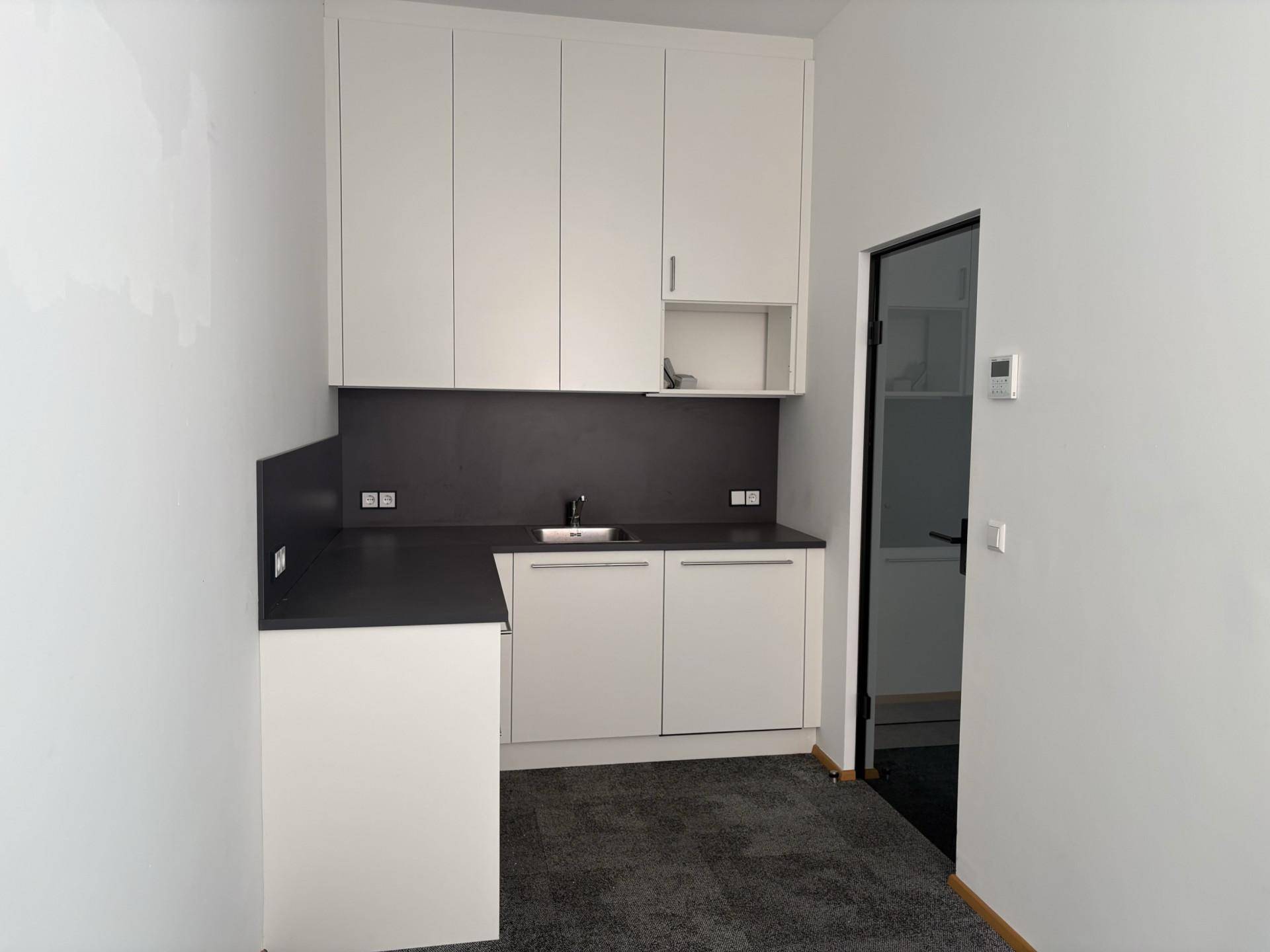 Moderne Küchenzeile mit weißen Schränken, dunkler Arbeitsplatte und integriertem Spülbecken in einem hellen Raum.