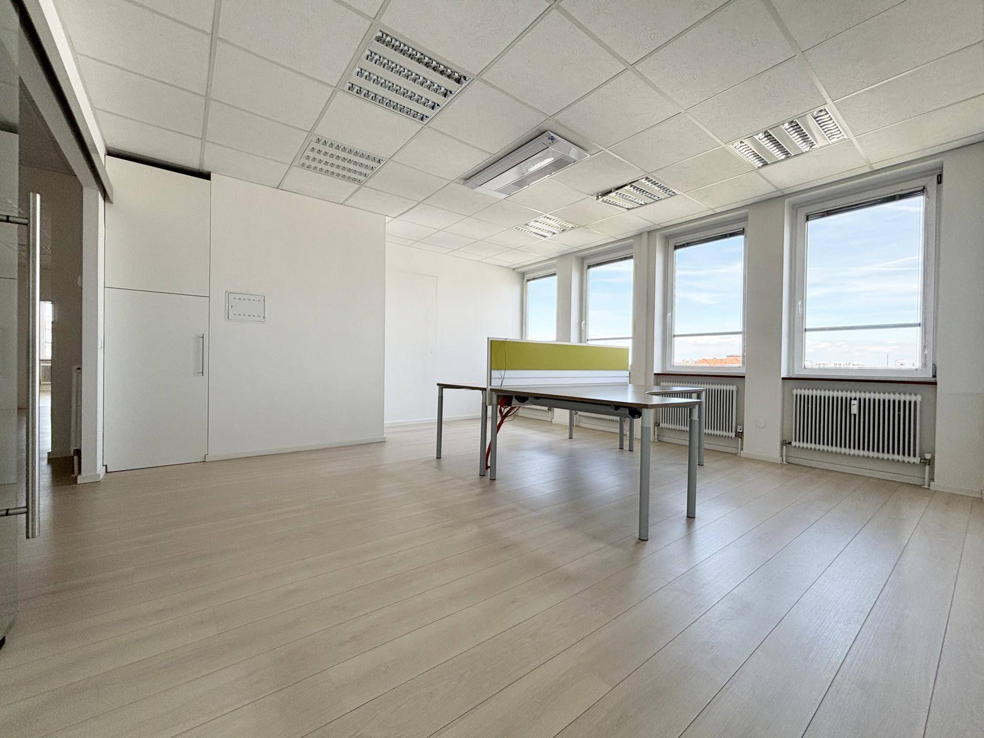 Großzügiges Büro mit holzbodenähnlichem Laminat, vielen Fenstern und modernen Büromöbeln.