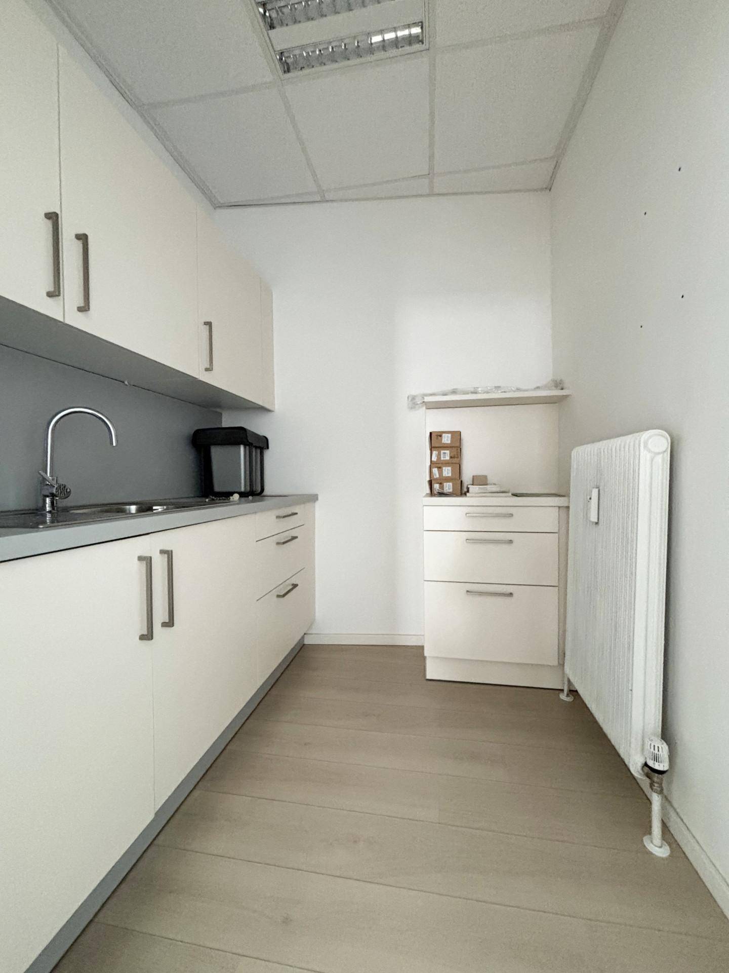Kleine, funktionale Küchenzeile mit weißen Schränken, Spüle und hellem Laminatboden.