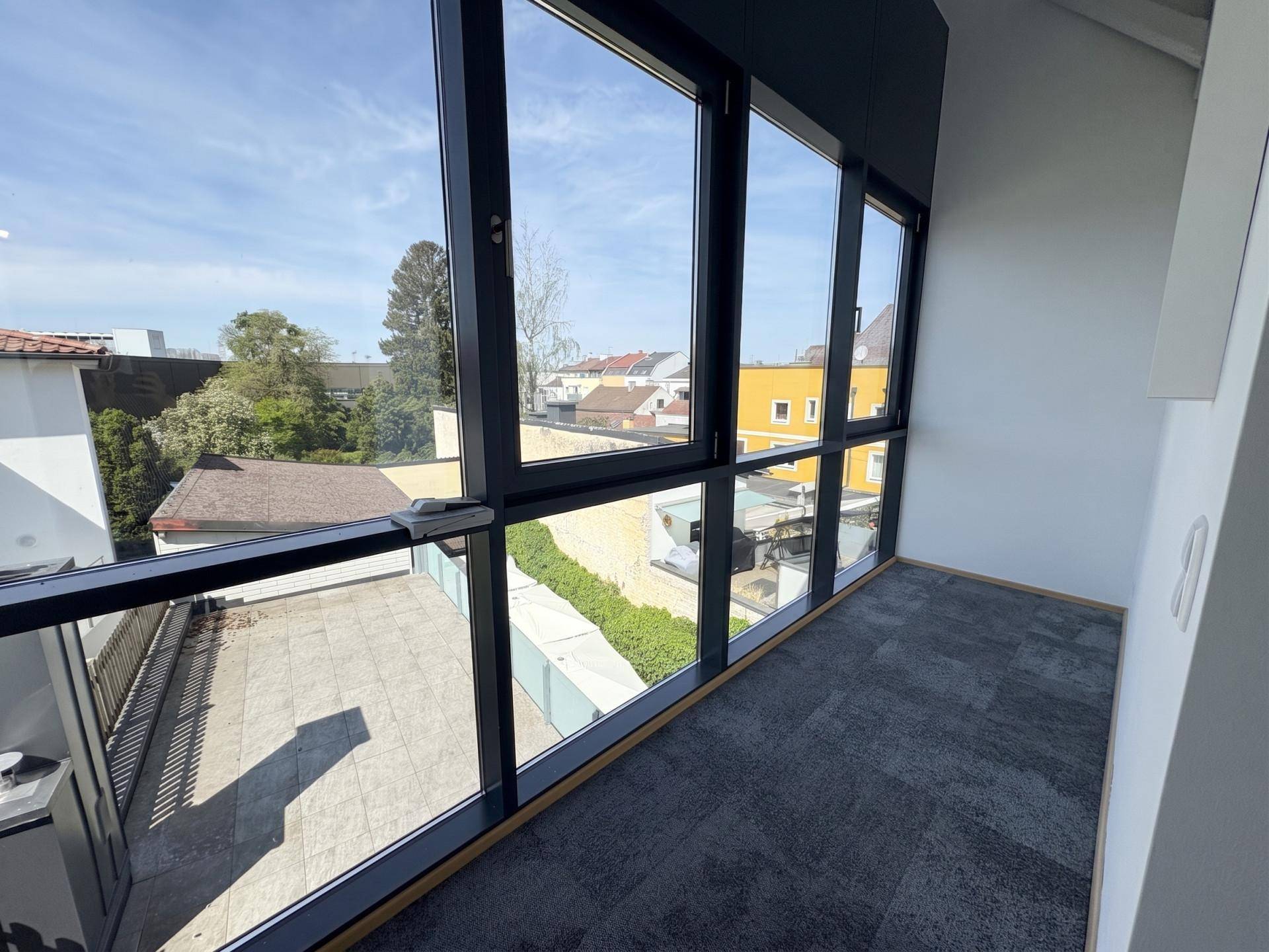 Innenansicht eines Büroraums mit großen Panoramafenstern, die einen weiten Blick auf die Terrasse bieten.