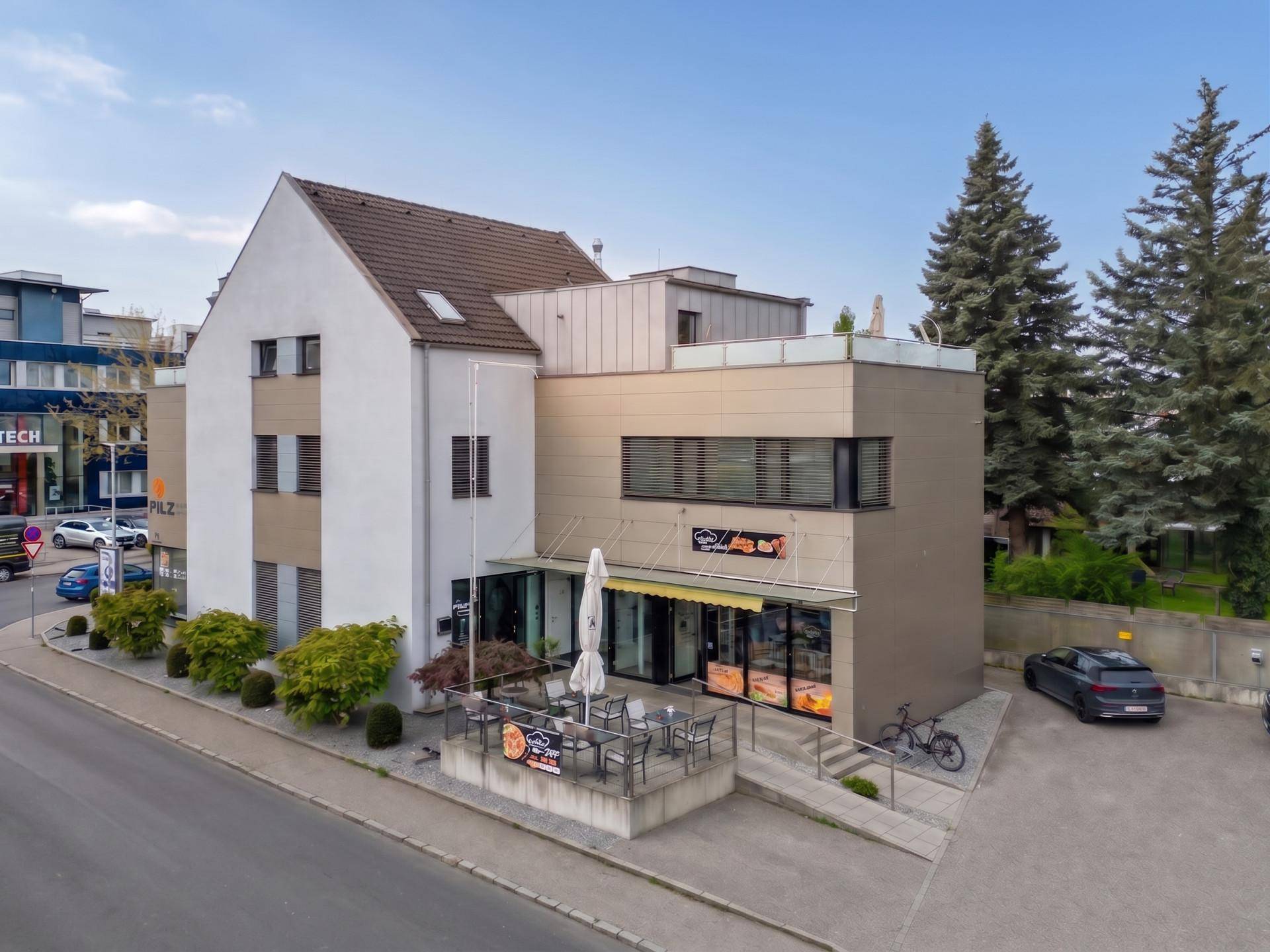 Gebäudeansicht von der Straßenseite mit moderner Architektur, Geschäftsflächen und Außenbereich.