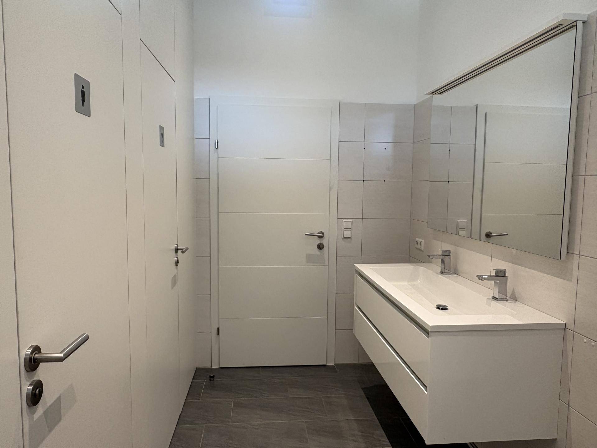 Modernes Badezimmer mit zwei Waschbecken, großem Spiegel und hellgrauen Fliesen an Wänden und Boden.