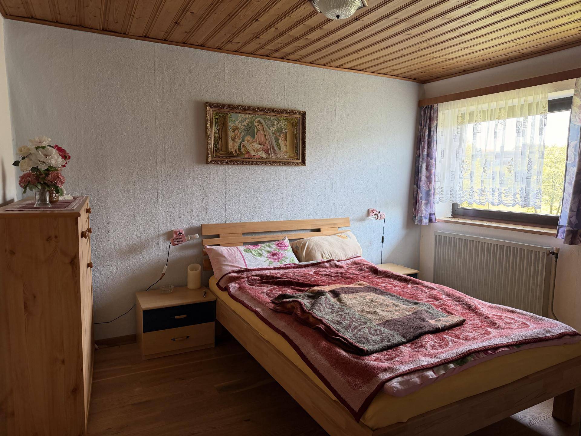 Gemütliches Schlafzimmer mit Doppelbett, Holzmöbeln und Blick auf die grüne Umgebung.