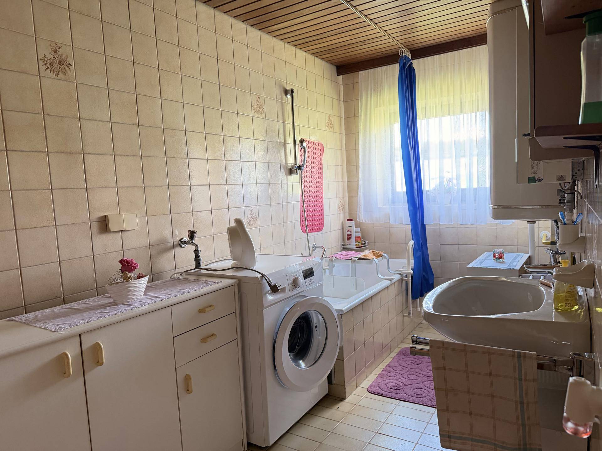 Funktionales Badezimmer mit Badewanne, Waschmaschine und Fliesen an Wänden und Boden.