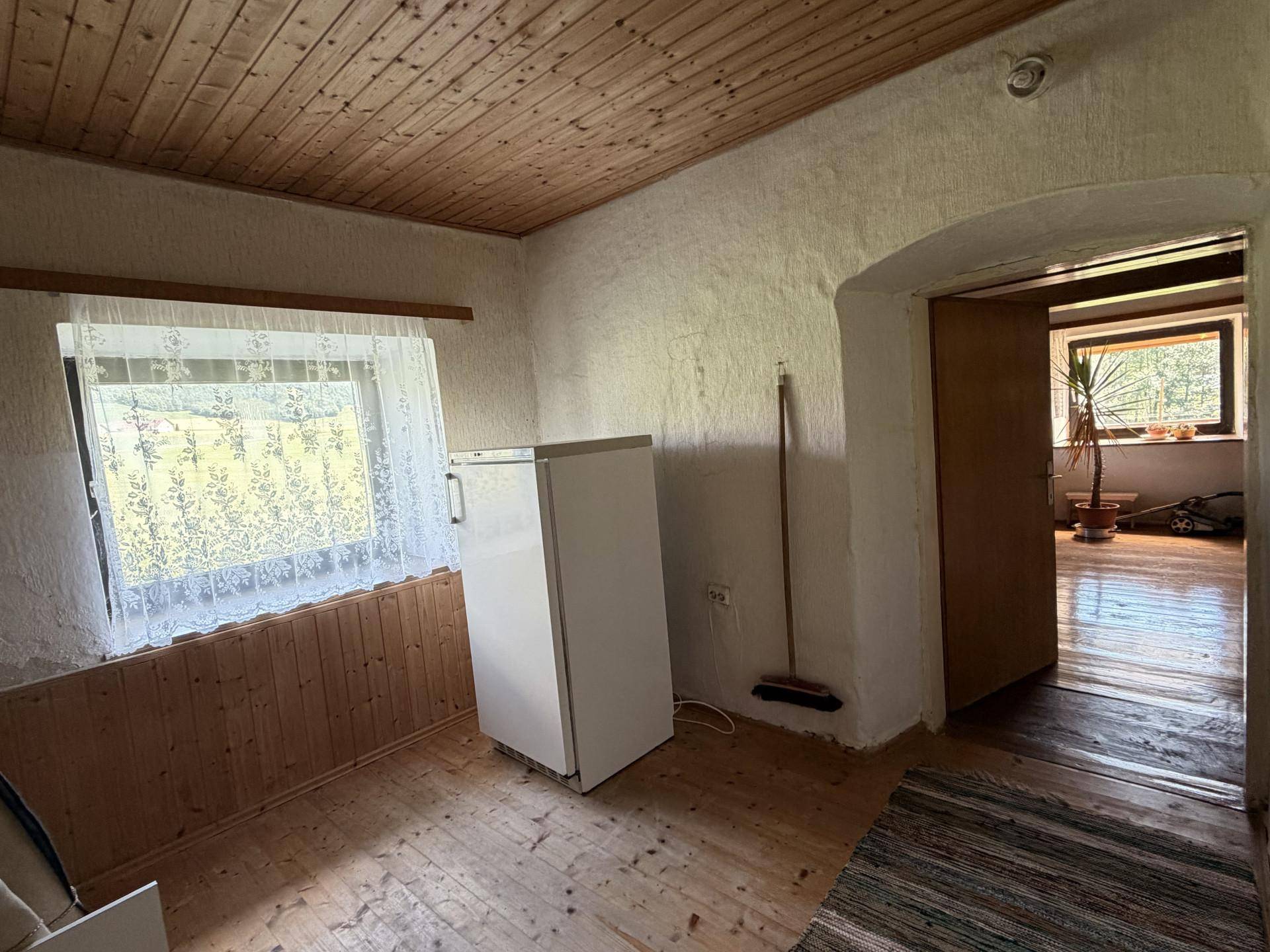 Einfacher Raum mit Holzboden und Fenster, der als Abstellraum oder Speisekammer genutzt werden könnte.