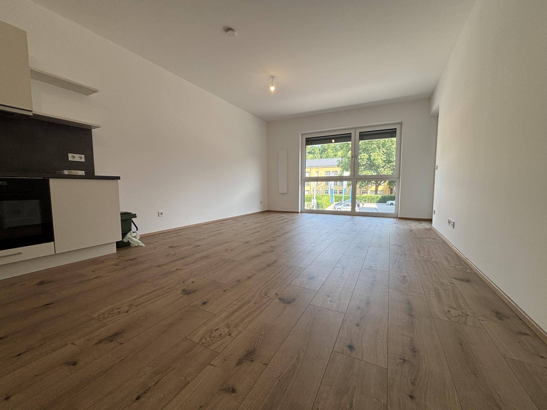 Heller Wohnbereich mit Holzboden und Blick ins Grüne durch das große Fenster.