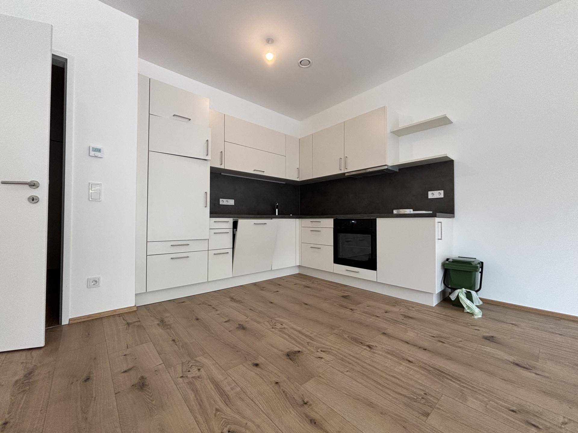 Moderne Einbauküche in Weiß mit dunkler Arbeitsplatte und integriertem Backofen.