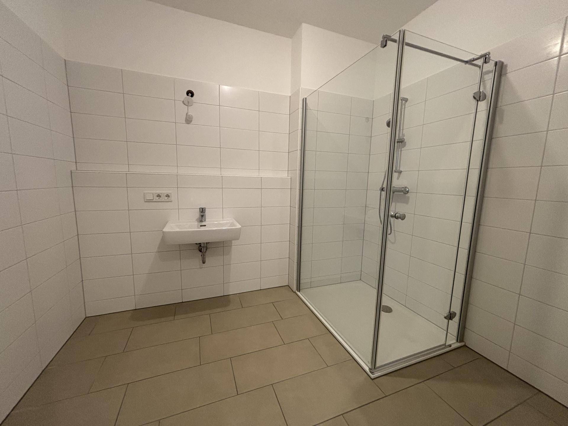 Modernes Badezimmer mit weiß gefliesten Wänden, Dusche und kleinem Waschbecken.