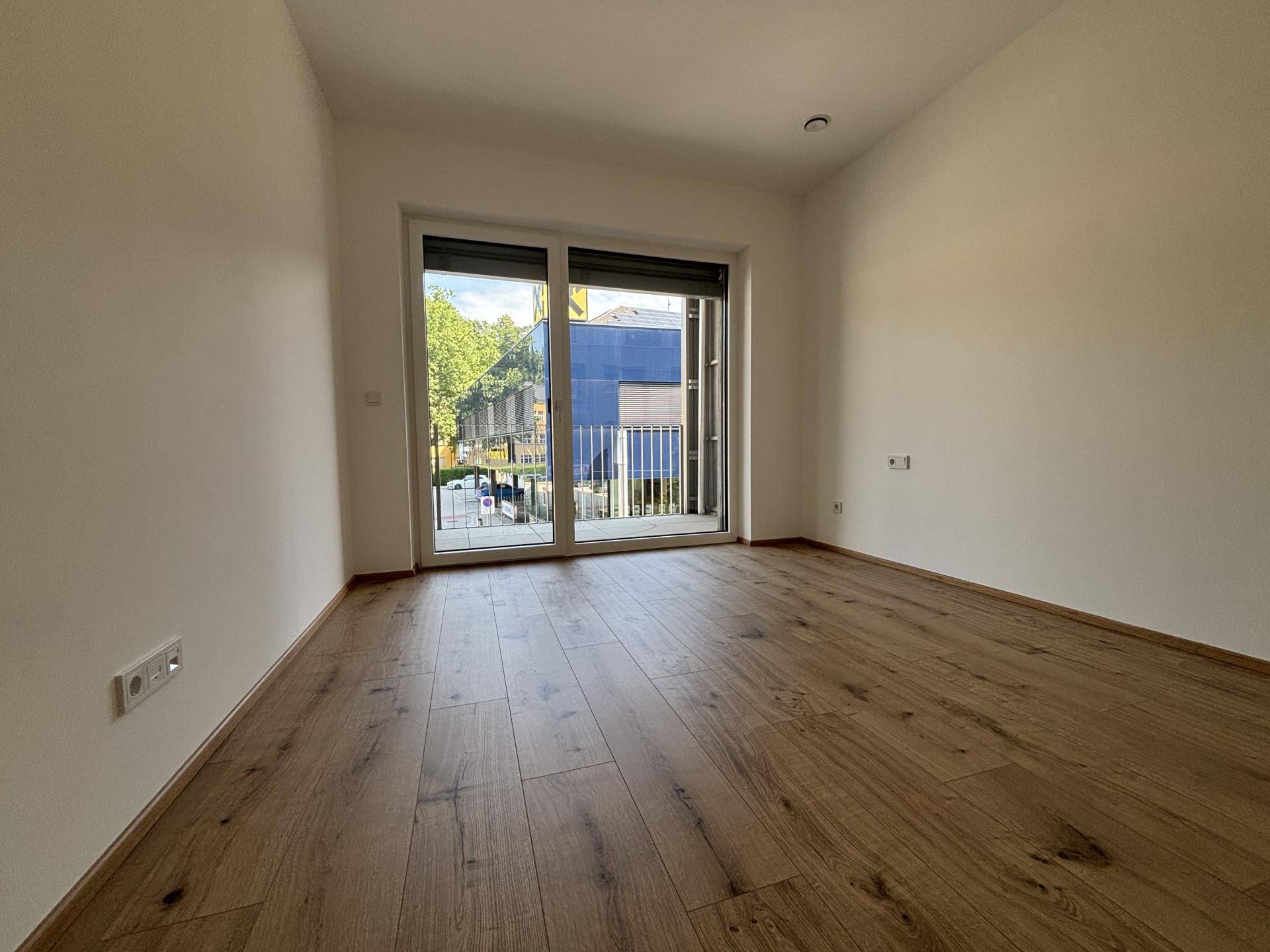 Helles Zimmer mit Holzboden und Zugang zu einem Balkon, ideal als Schlafzimmer.