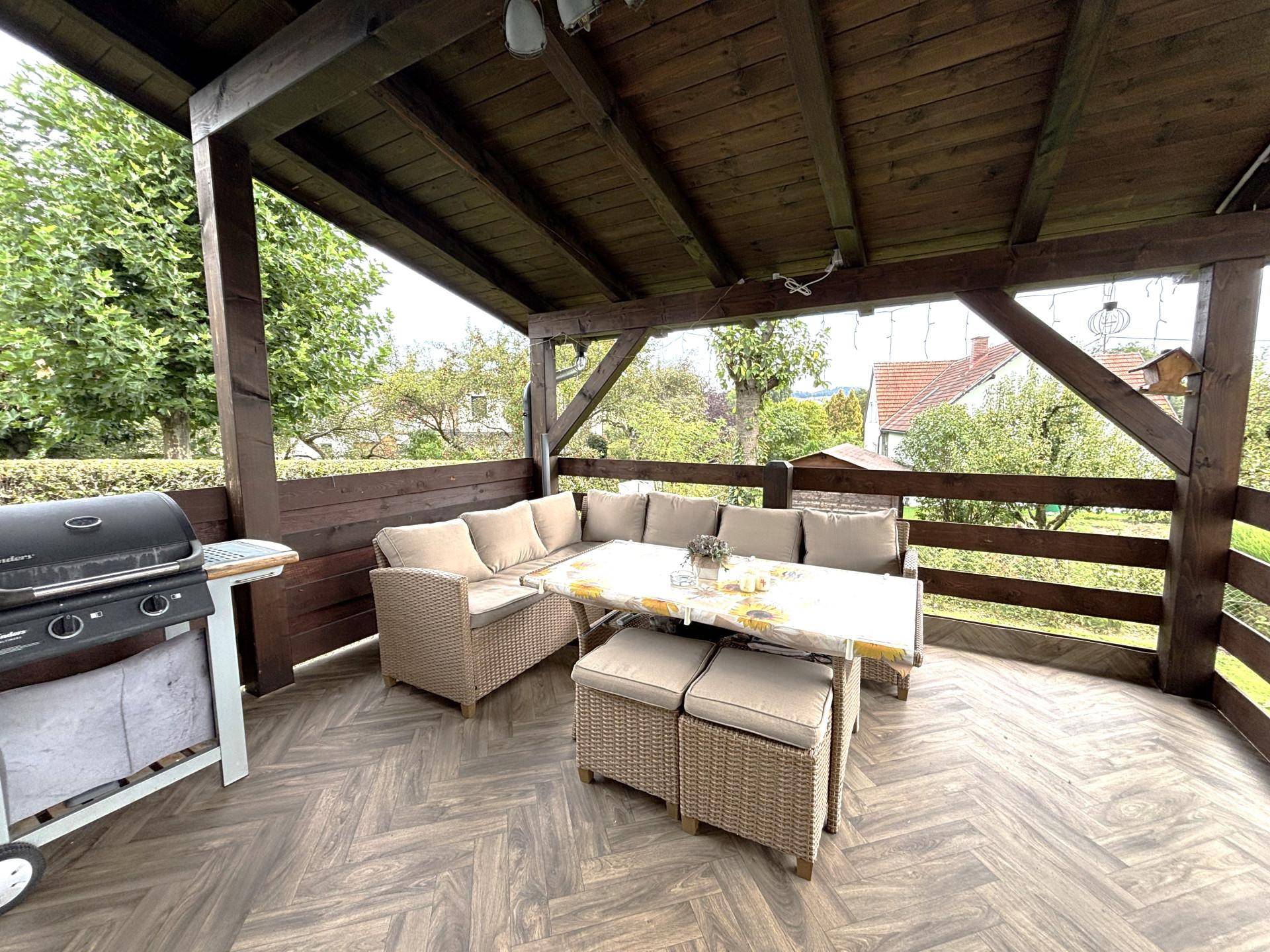Überdachte Terrasse mit gemütlicher Sitzgruppe, Grill und Holzbalkenkonstruktion.