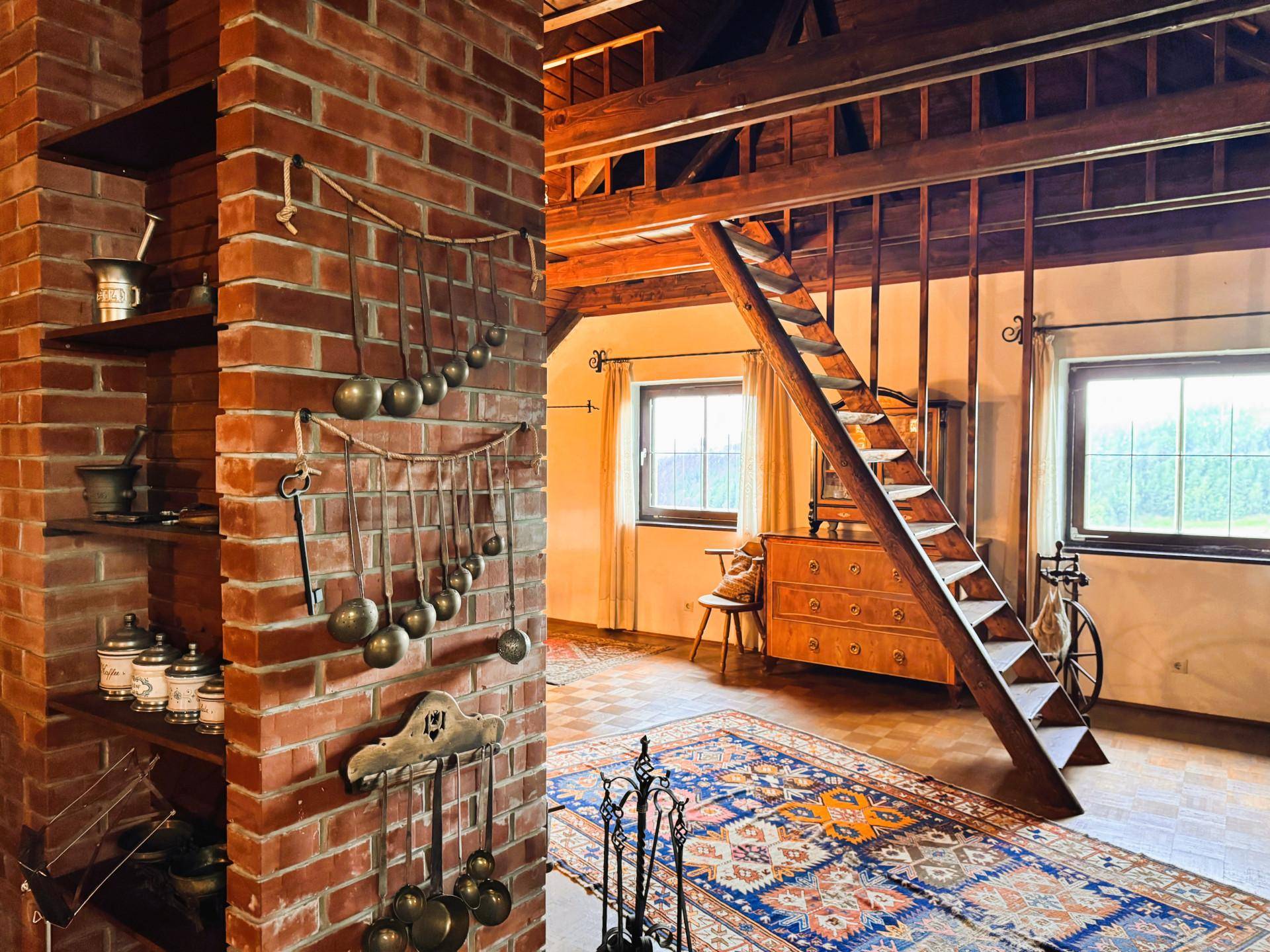 Rustikaler Wohnbereich mit freiliegender Ziegelwand, Holztreppe und traditionellen Einrichtungsgegenständen.