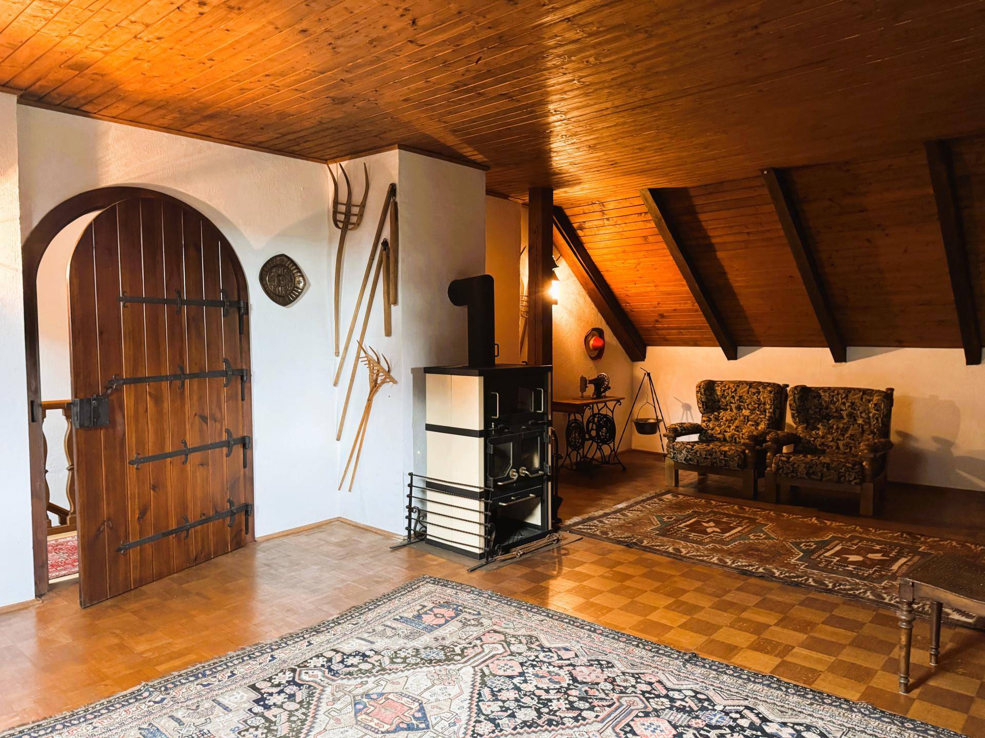 Großer Wohnbereich mit Holzbalkendecke, traditionellem Ofen und rustikaler Holztür.