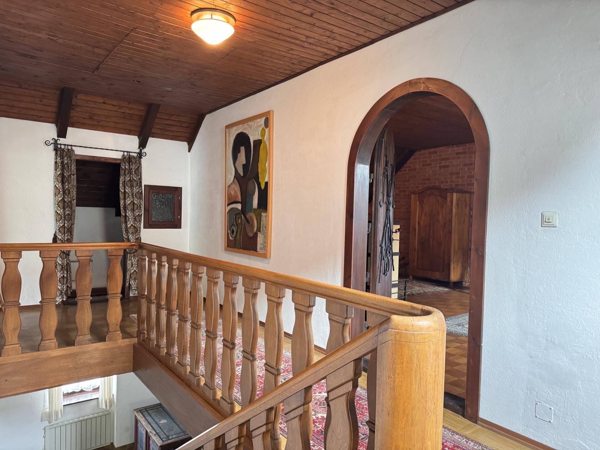 Treppenhaus mit Holzgeländer, Holzbalkendecke und traditioneller Kunst an der Wand.