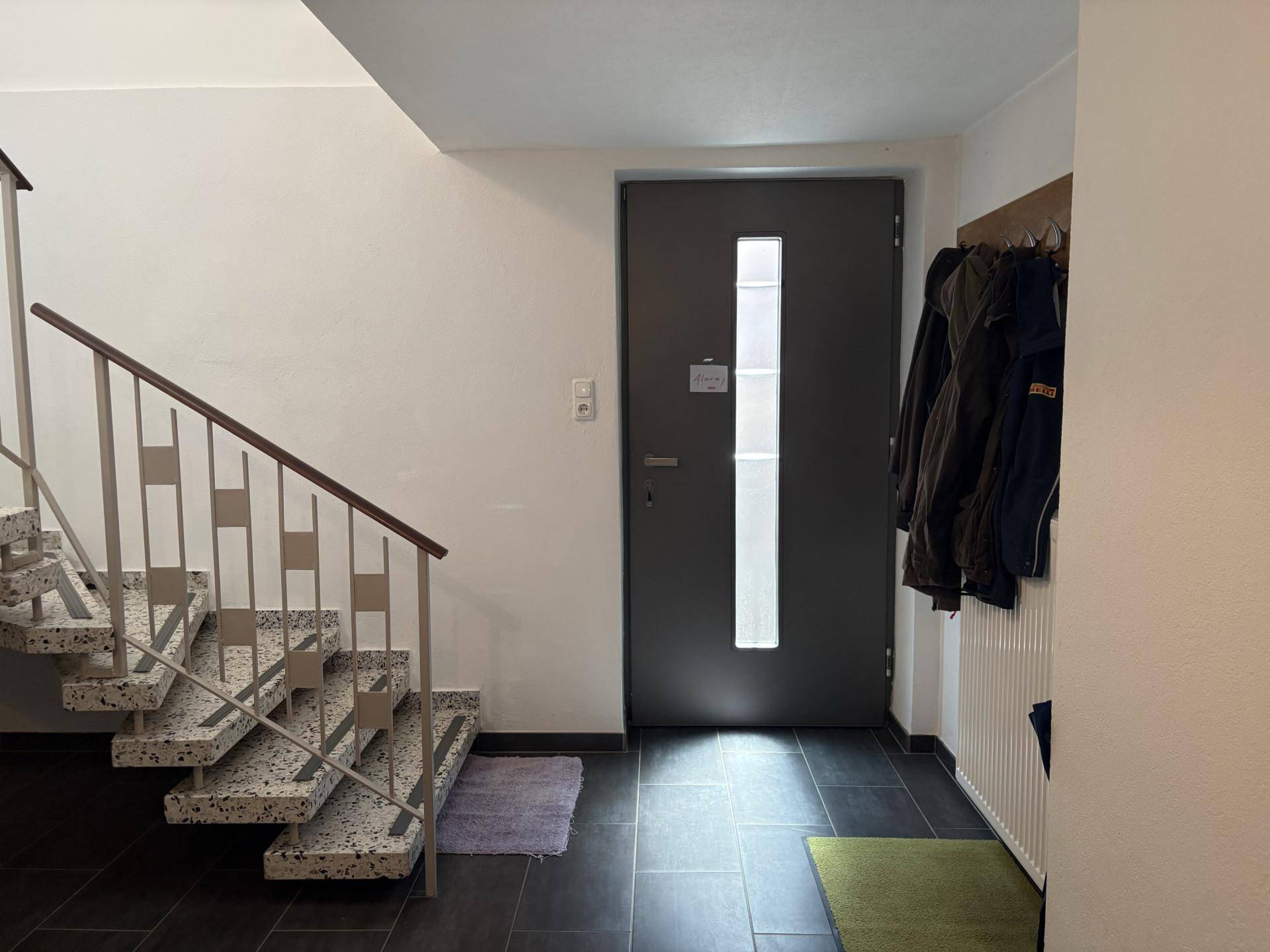 Eingangsbereich mit Treppe, dunklen Fliesen und Garderobe, einladend gestaltet.