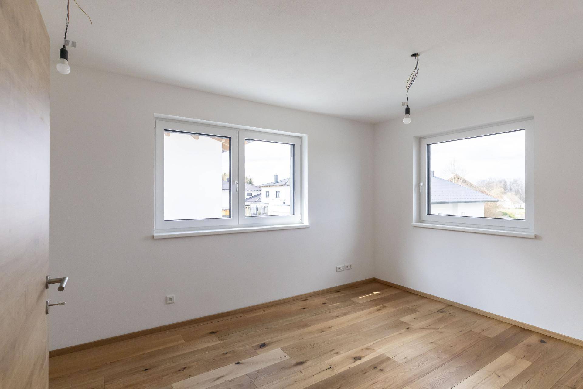 Helles Schlafzimmer mit Holzboden und zwei Fenstern, bereit für die individuelle Einrichtung.