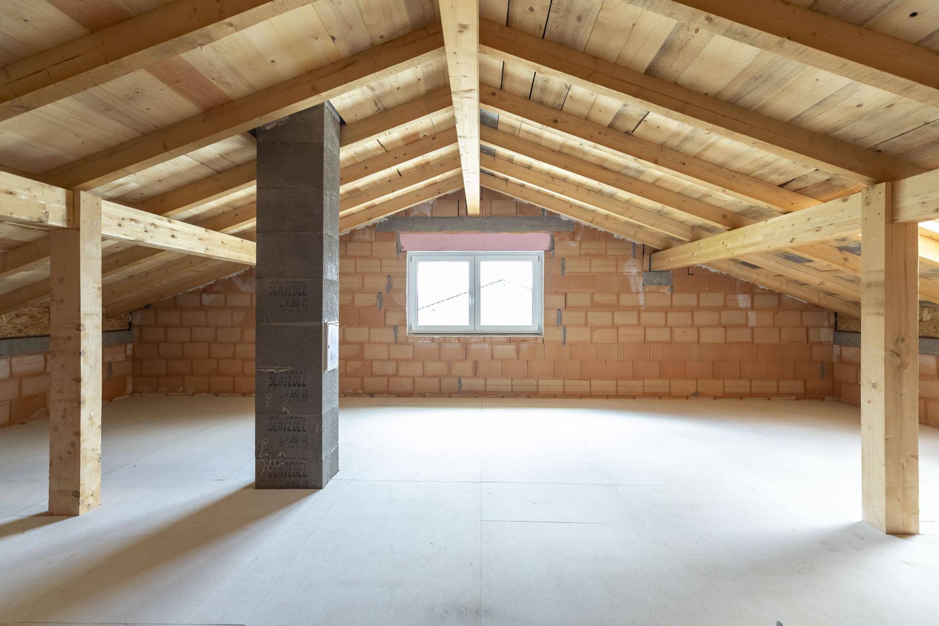 Geräumiger Dachboden mit sichtbaren Holzbalken und Ziegelwänden, bereit für den Ausbau.