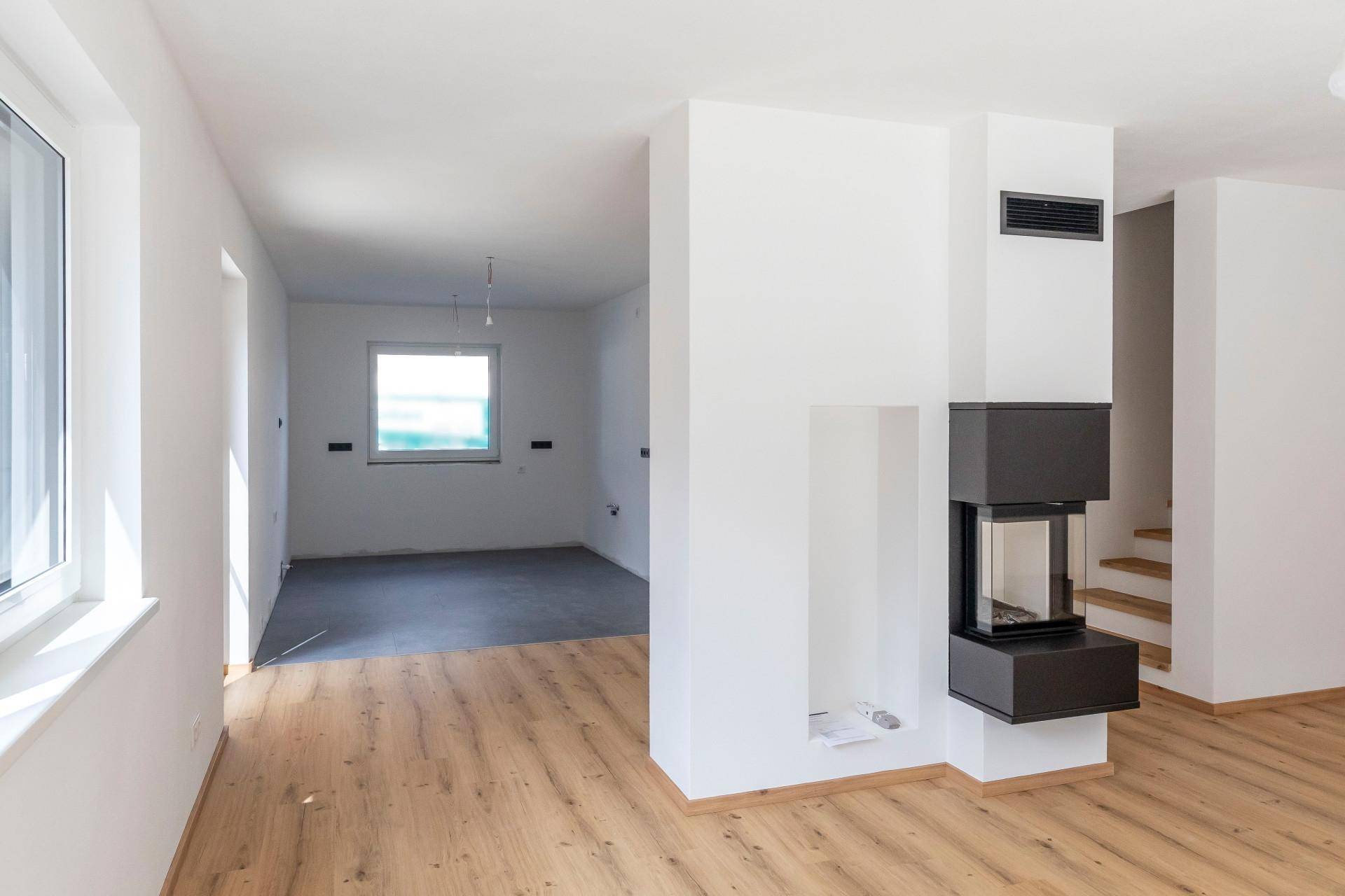 Heller Wohnbereich mit modernem Kamin und Holzboden, offen zu einem weiteren Raum.