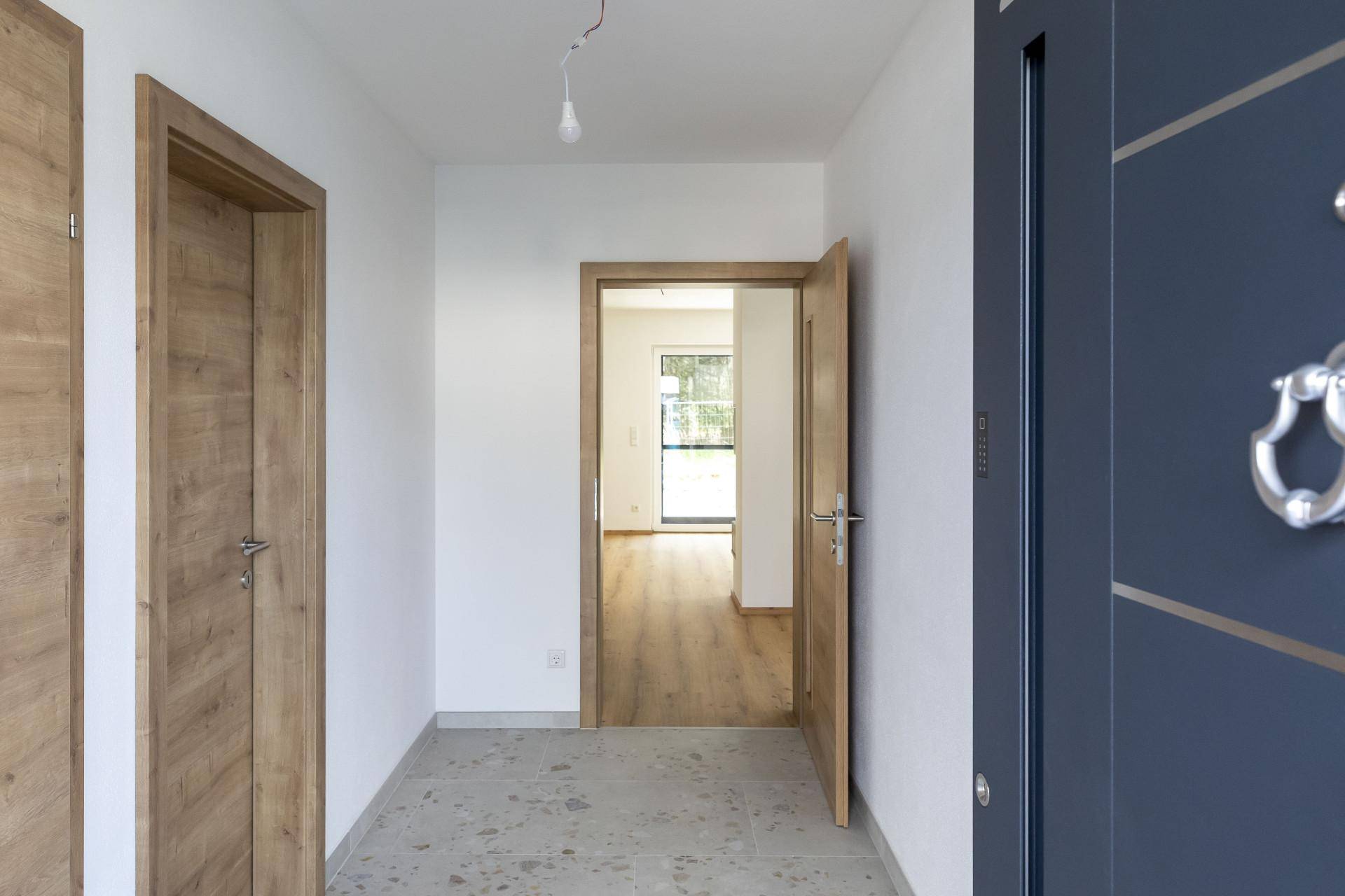 Heller Eingangsbereich mit moderner Haustür, Holztüren und Fliesenboden, Blick in den Wohnbereich.