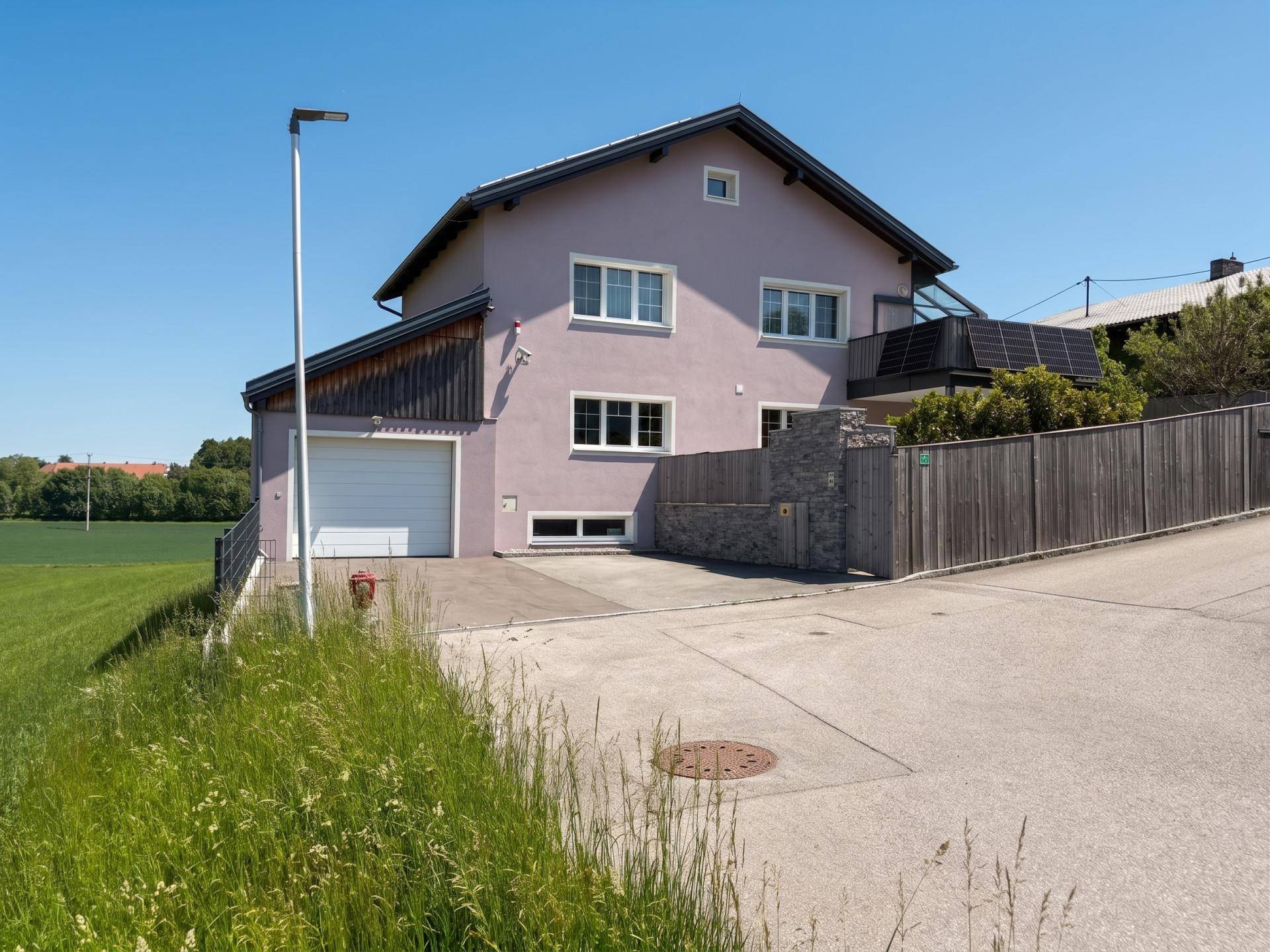 Ansicht des Hauses von der Seite mit Garage und Zufahrt, umgeben von grünen Feldern.