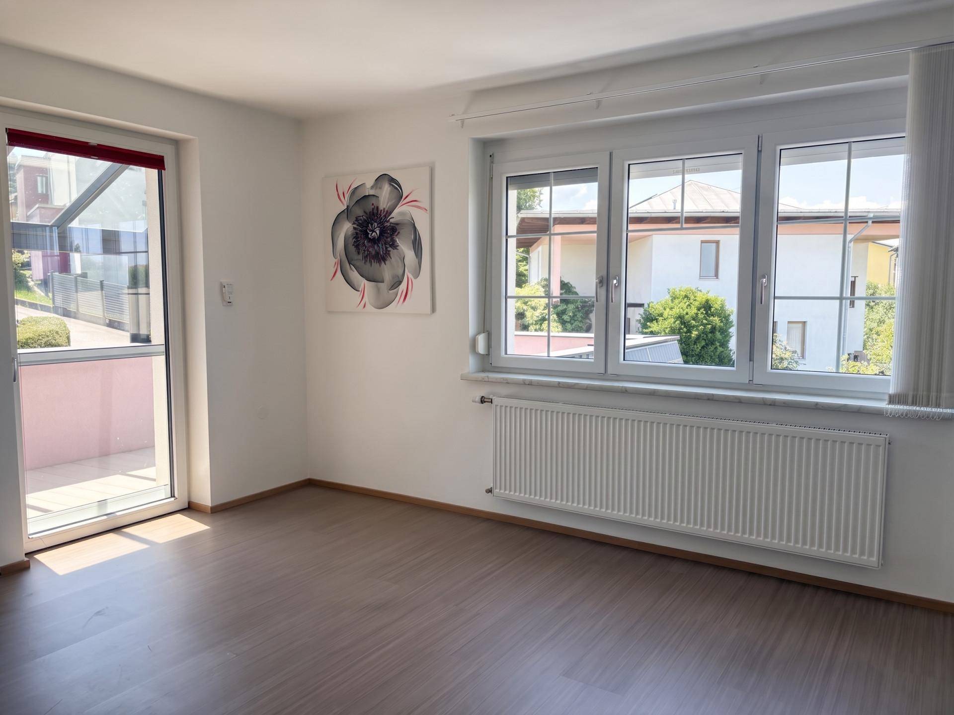 Heller Raum mit Laminatboden, großen Fenstern und Zugang zu einem Außenbereich.