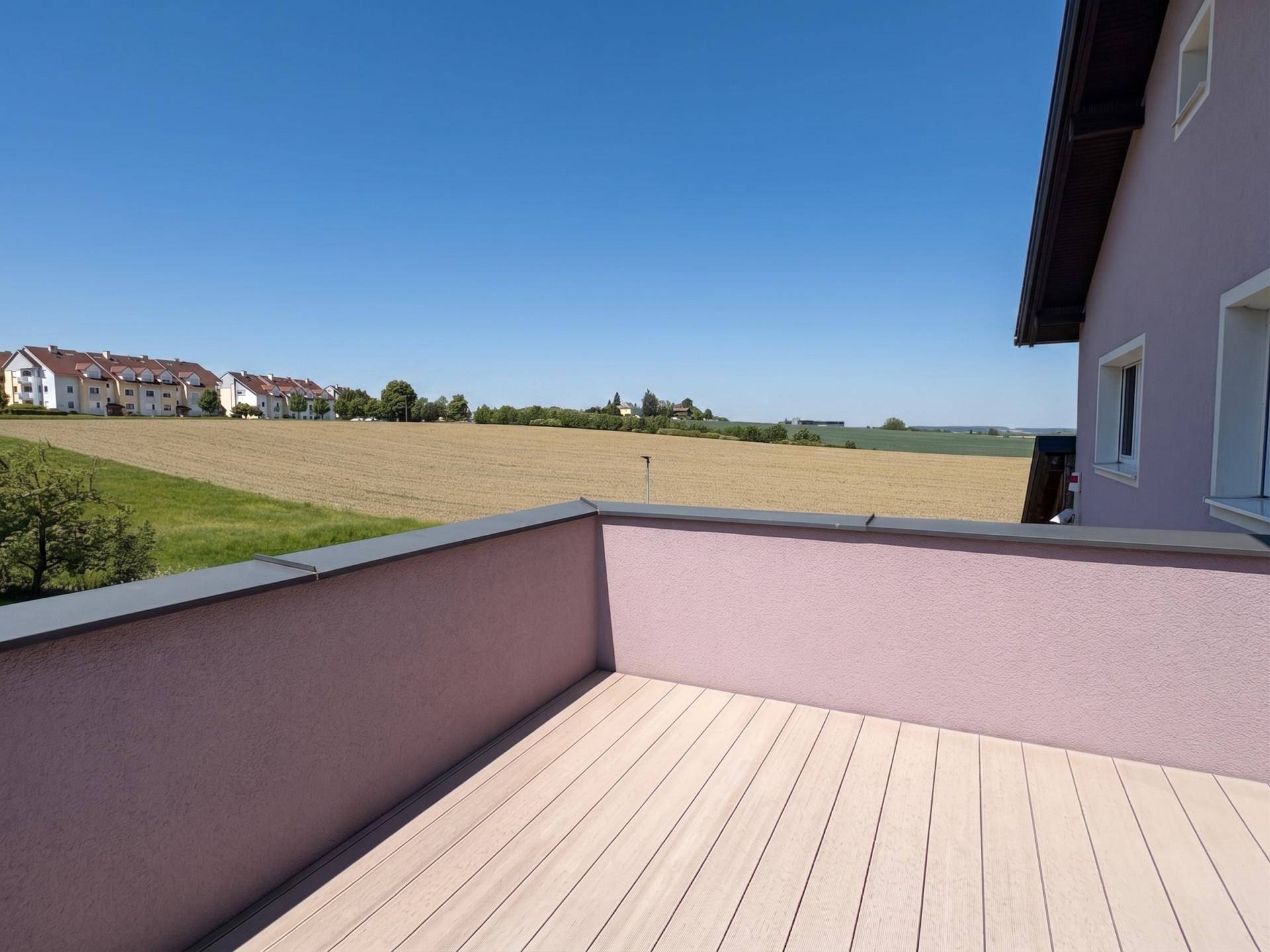 Geräumiger Balkon mit Holzdielen und weitem Blick über Felder und die Nachbarschaft.