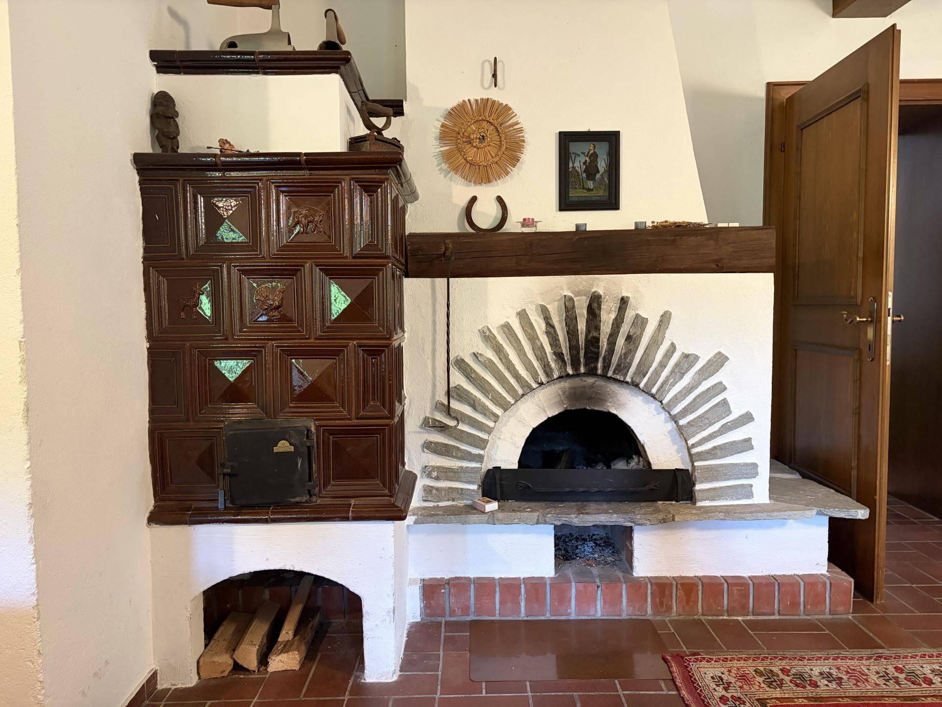 Rustikaler Kaminbereich mit traditionellem Kachelofen und gemauertem Brotbackofen, ideal für gemütliche Abende.