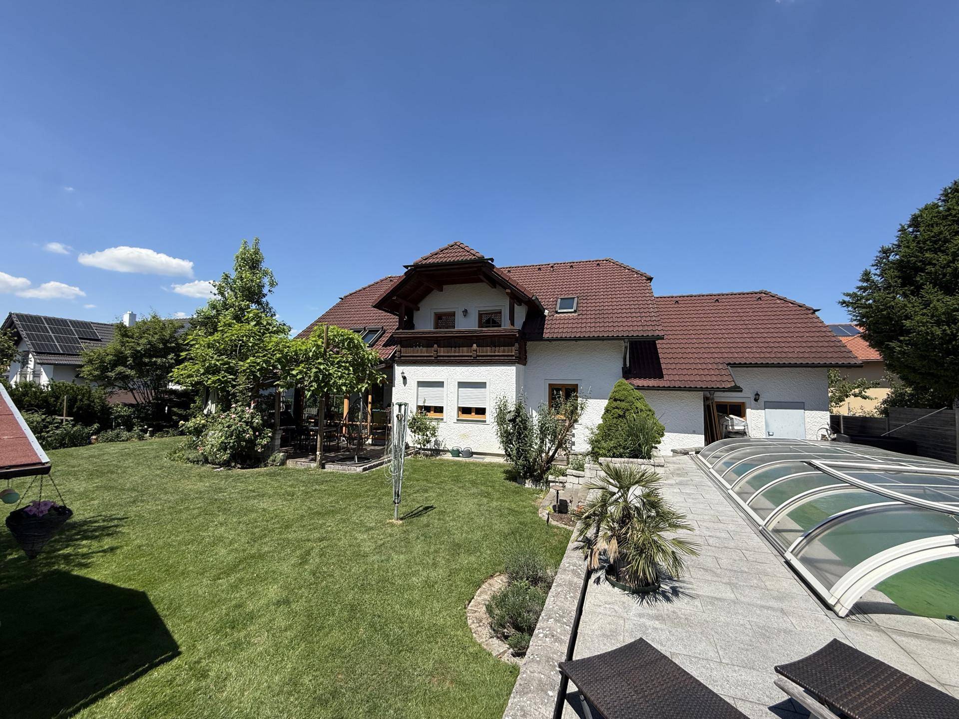 Weitläufiger Garten mit Poolbereich, Liegeflächen und dem Wohnhaus unter strahlend blauem Himmel.