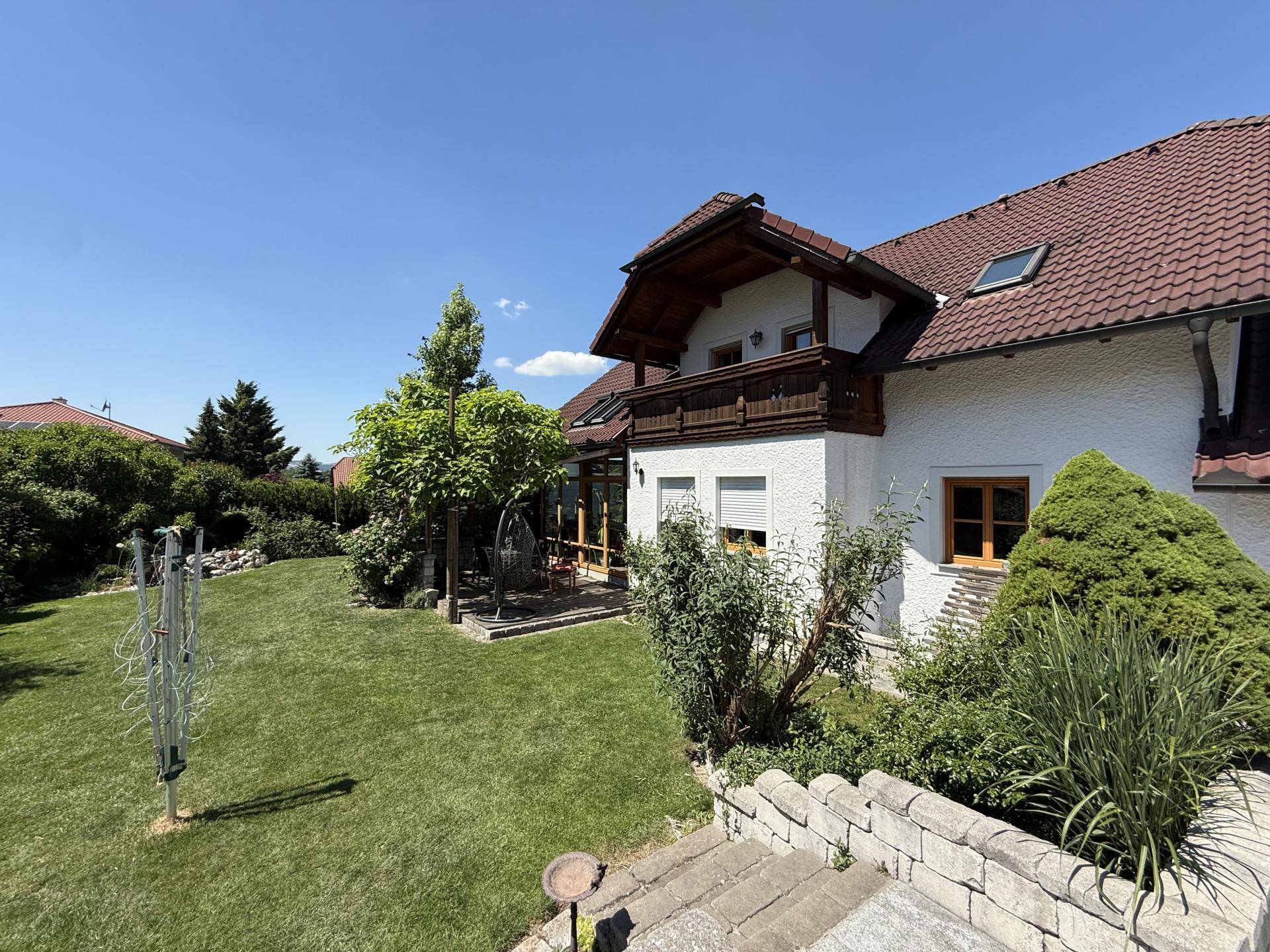 Seitlicher Blick auf das Wohnhaus mit gepflegtem Garten, Rasenfläche und Steinmauer.