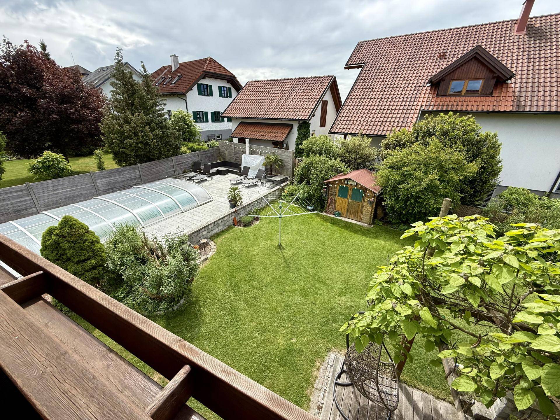 Weitläufiger Blick vom Balkon über den grünen Garten mit Pool und umliegende Häuser.