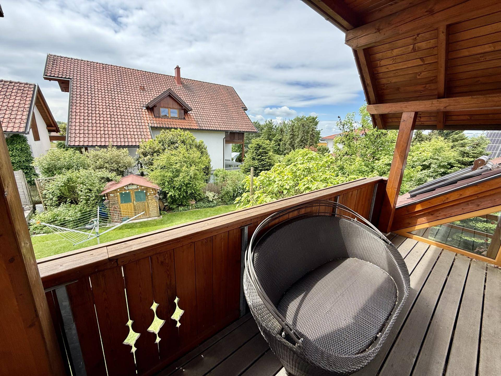 Balkon mit Holzboden und dekorativem Geländer, bietet einen Ausblick auf die grüne Umgebung.