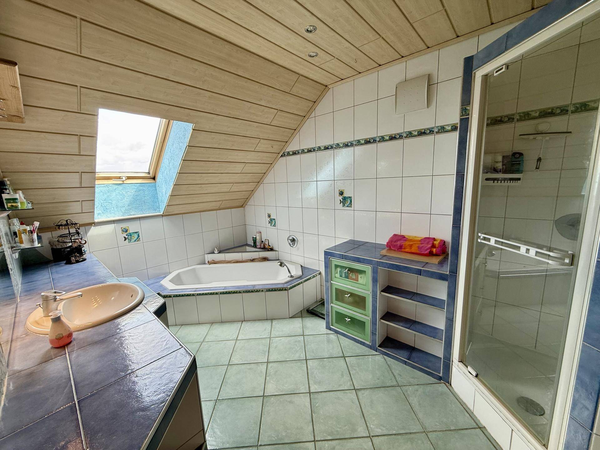Badezimmer im Dachgeschoss mit blauen Fliesen, Badewanne, Dusche und Dachfenster.